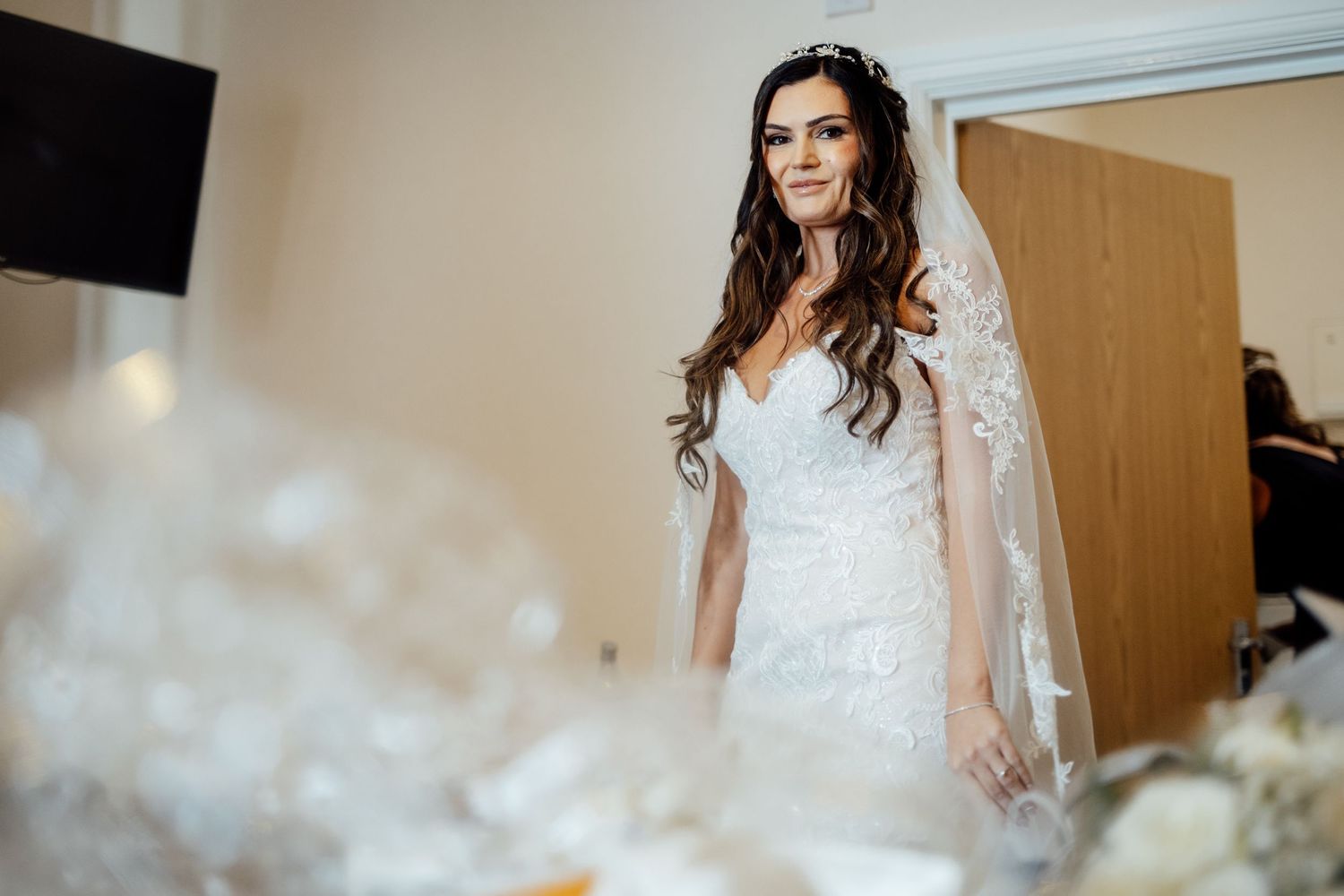 Bride in elegant lace wedding gown and veil standing in preparation room.