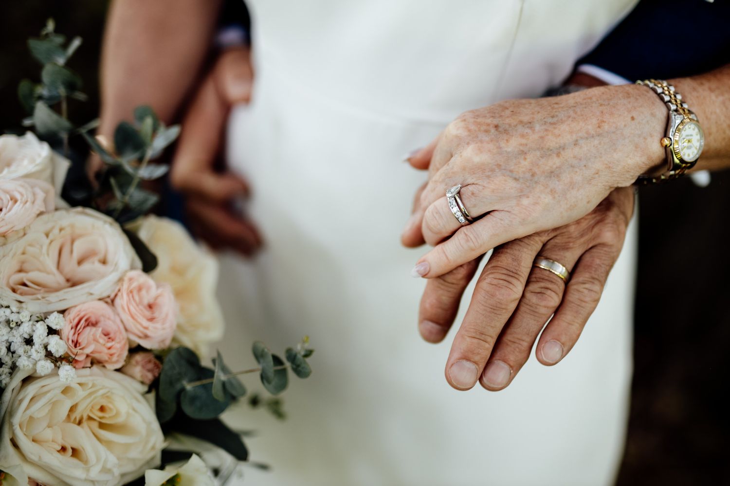 Close-up of wedding rings and delicate pink roses with greenery.