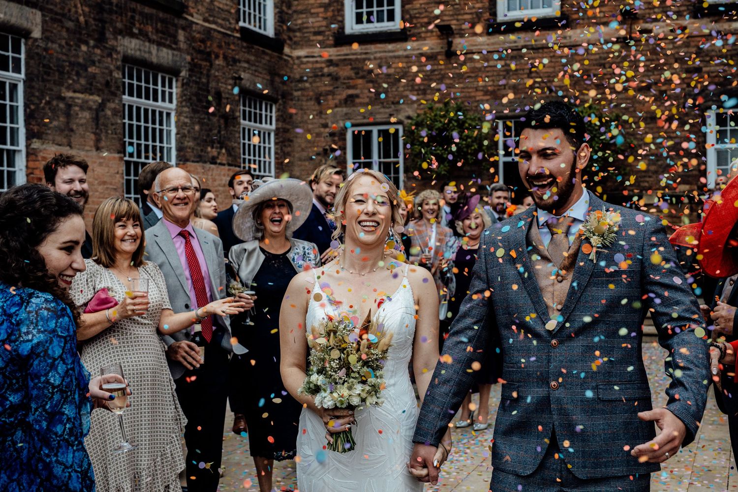 Wedding guests throwing confetti outside a historic brick building.