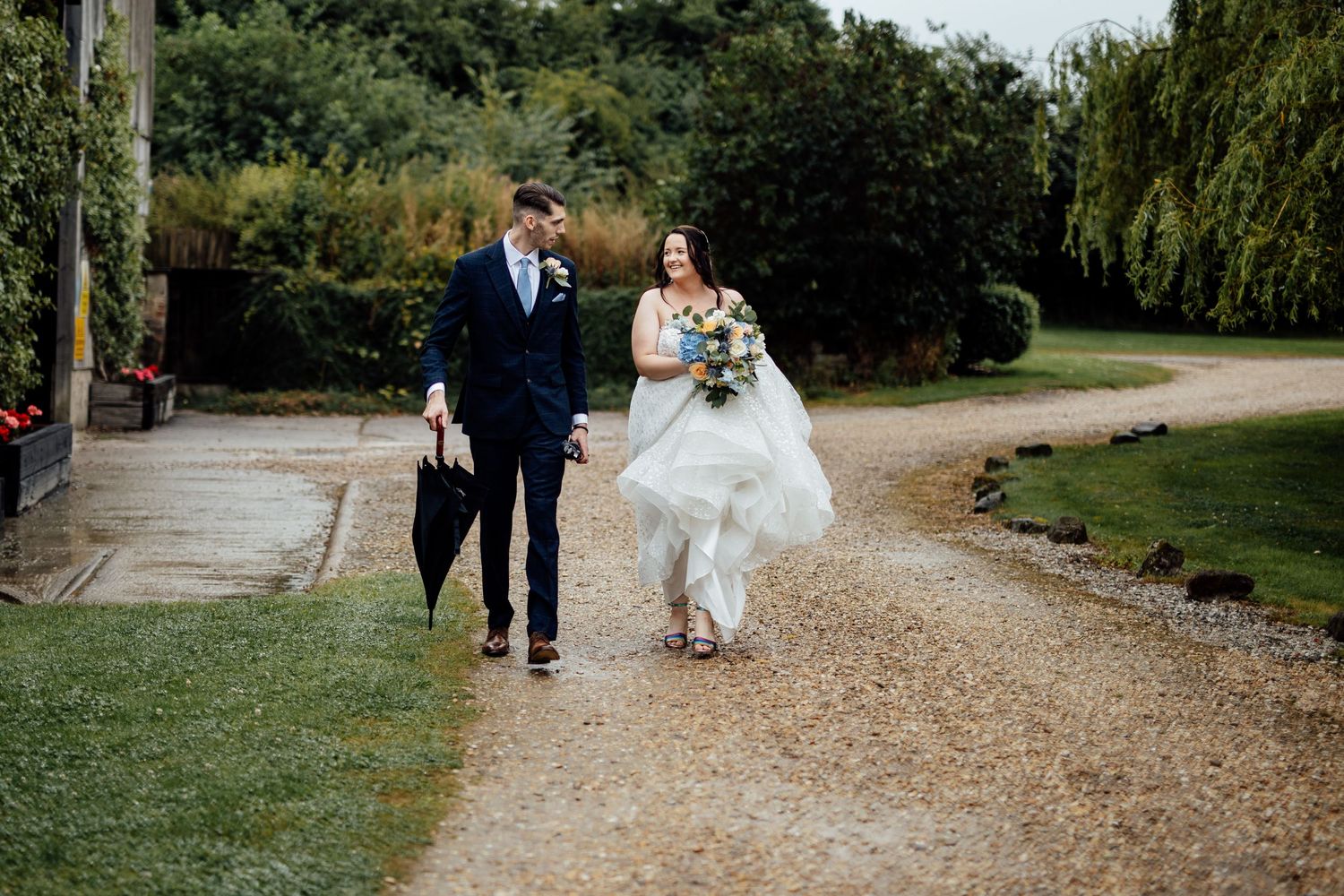 Newlyweds walking together on gravel path through garden setting.
