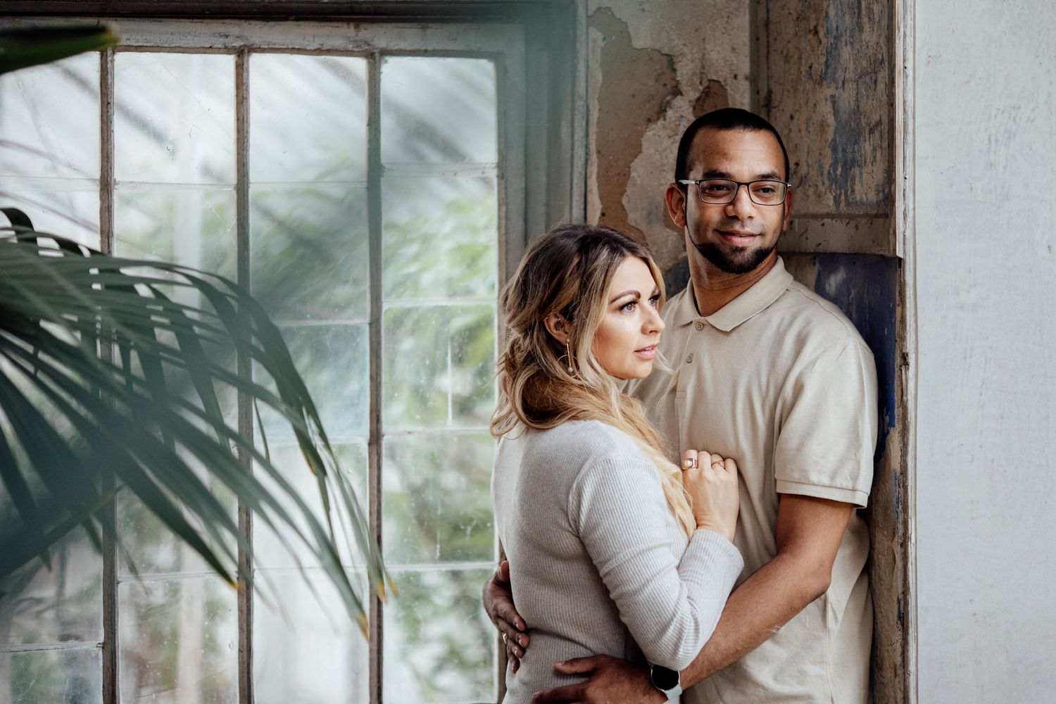 Intimate indoor photoshoot with soft natural lighting through windows and tropical plant shadows.