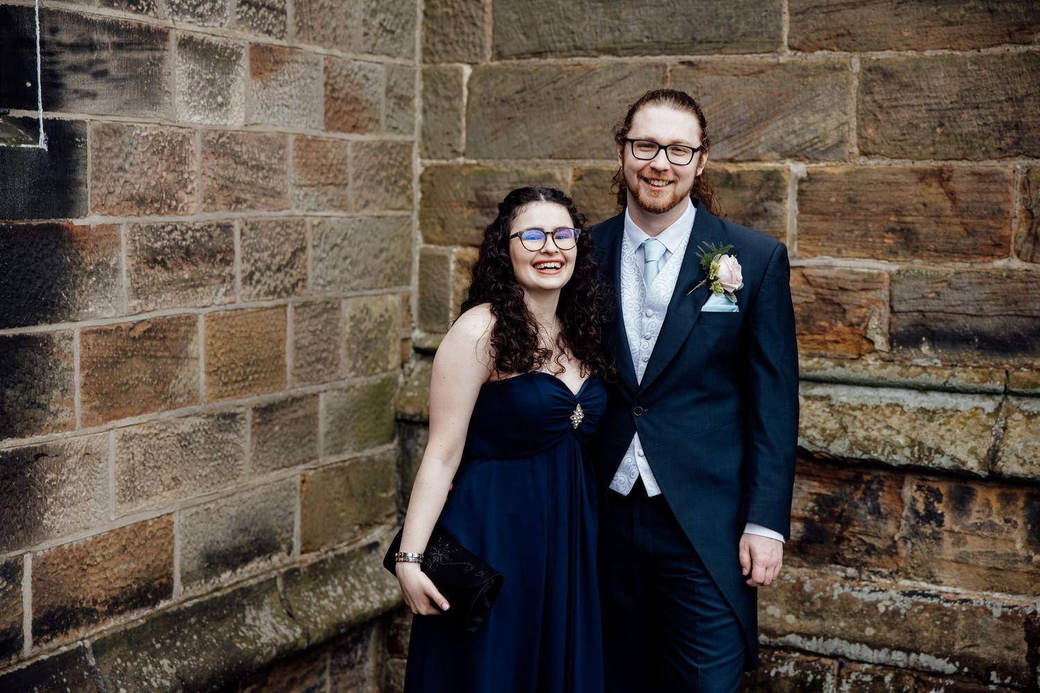 Formal wedding portraits taken against a stone wall background.
