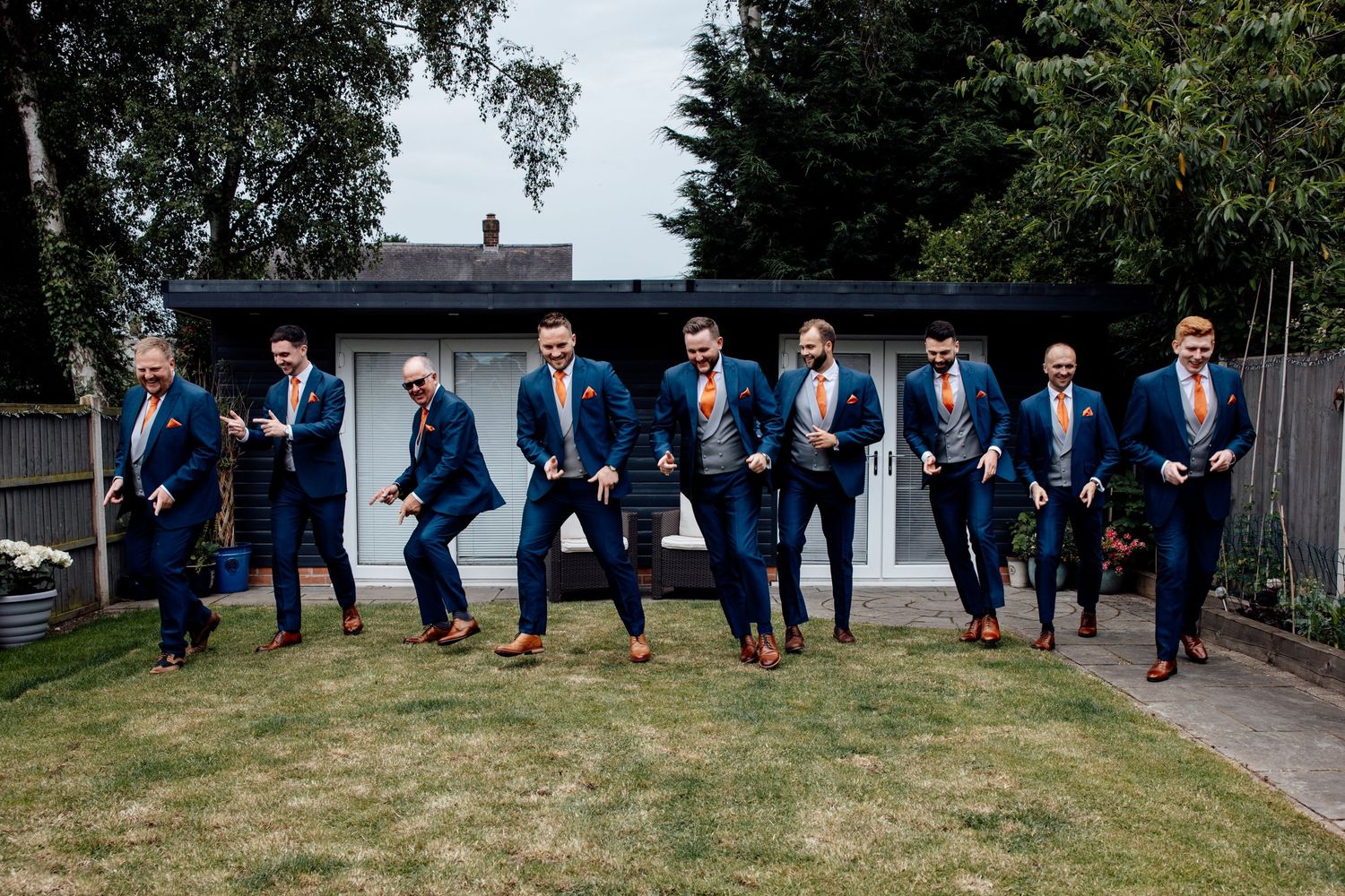 Groomsmen in matching navy blue suits pose together on a lawn.