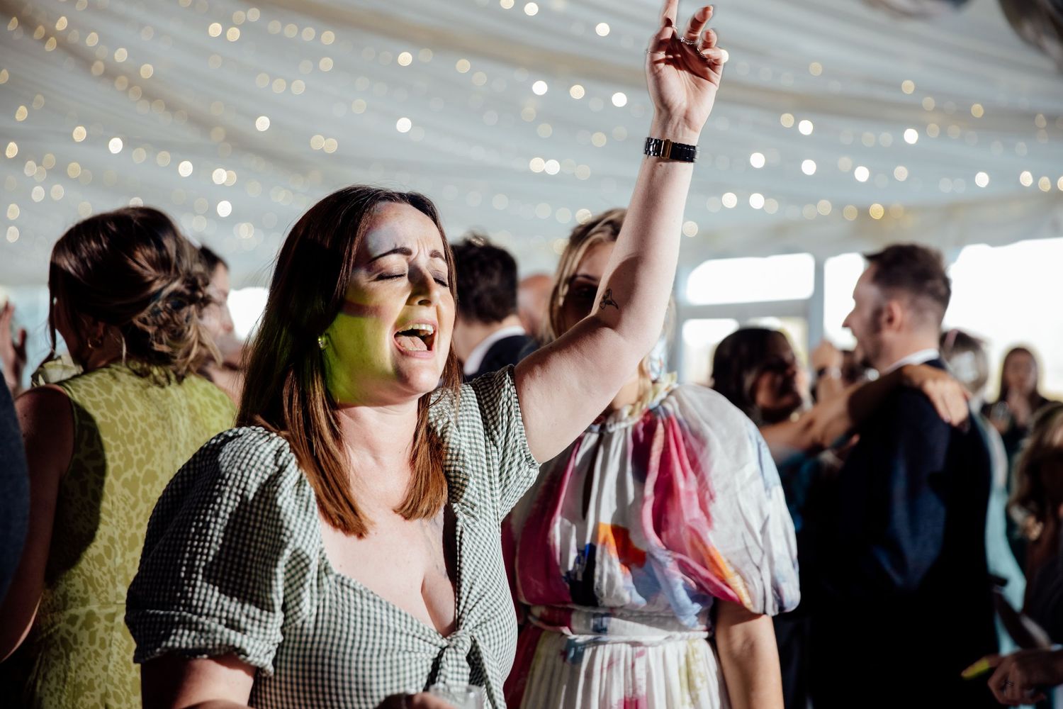 An energetic guest dancing at a wedding reception under string lights.