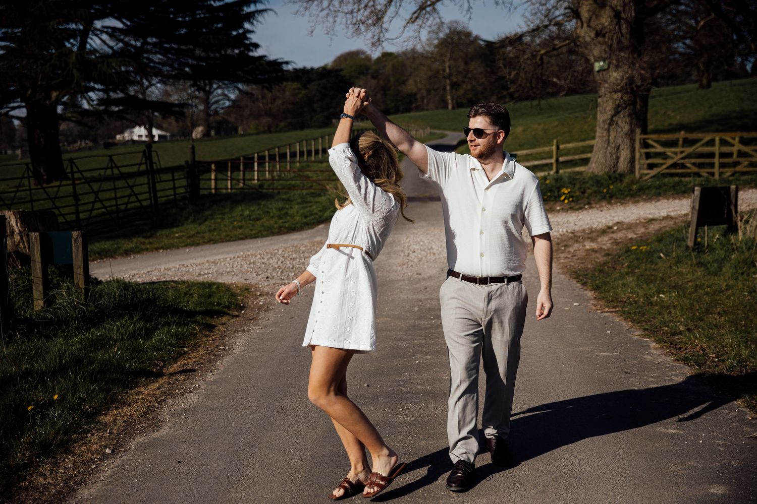 Two people in light colored outfits walk together on a winding country path.