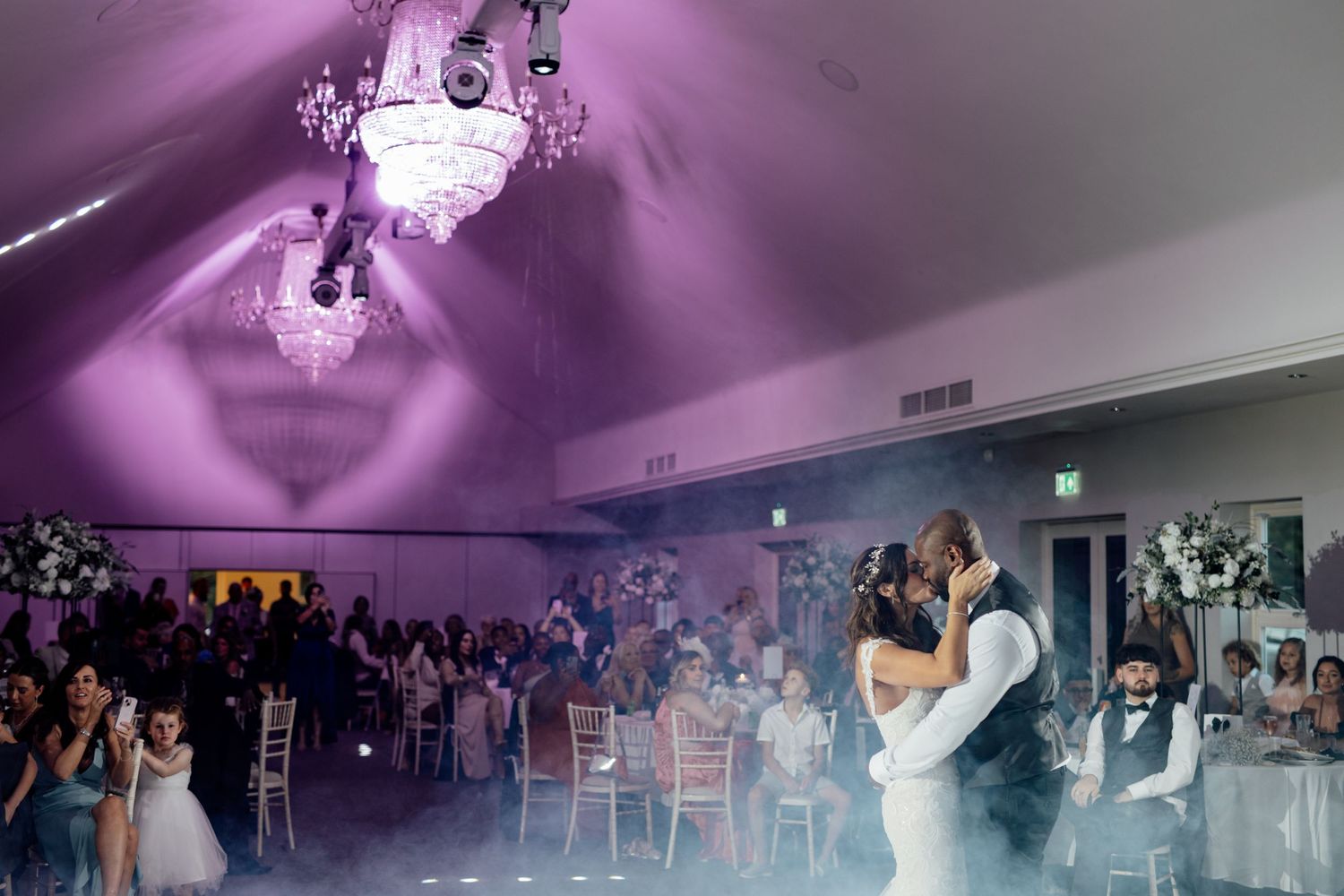Wedding reception venue with purple uplighting and guests dancing under vaulted ceiling.