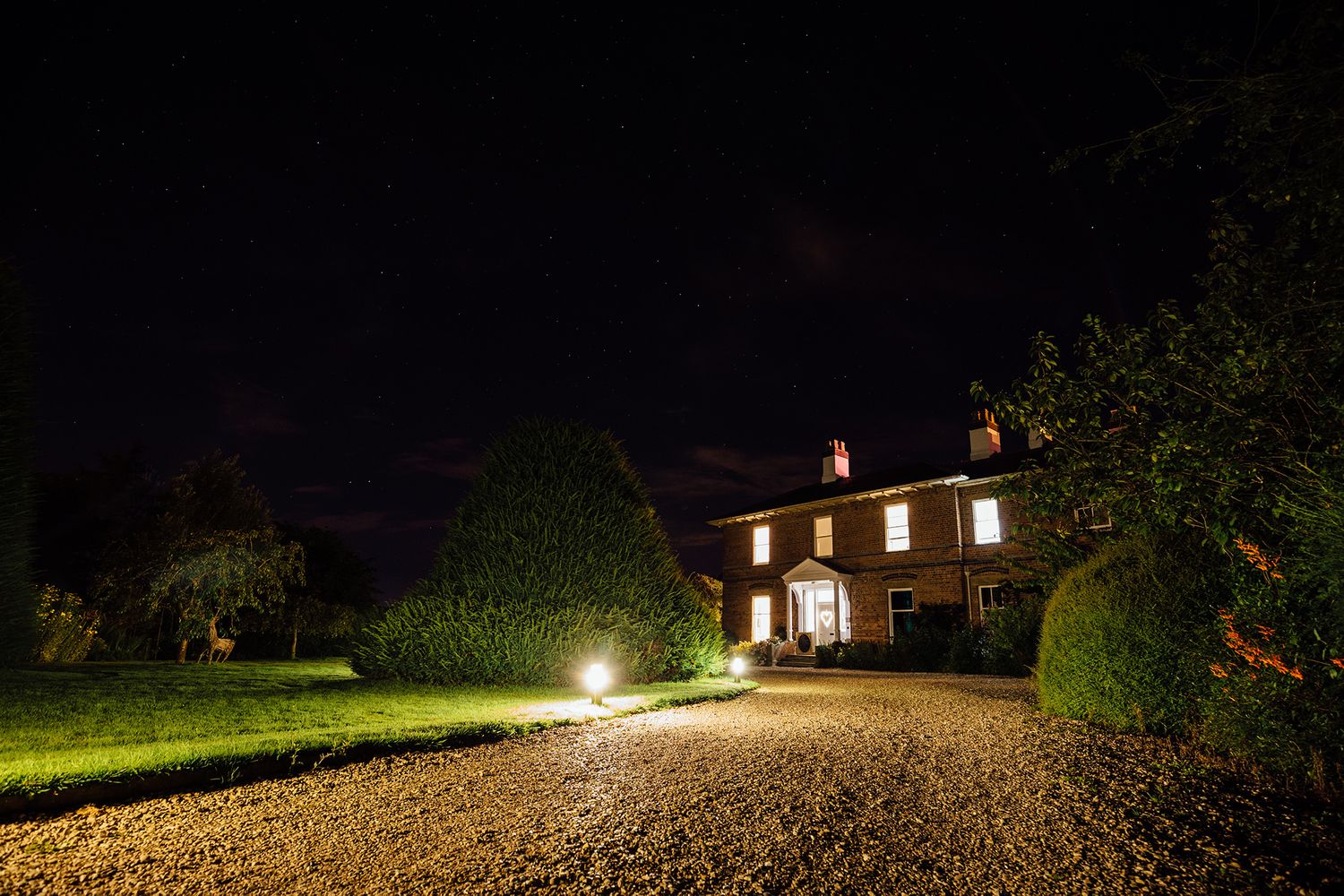Illuminated country house glows warmly against dark night sky during evening wedding reception.