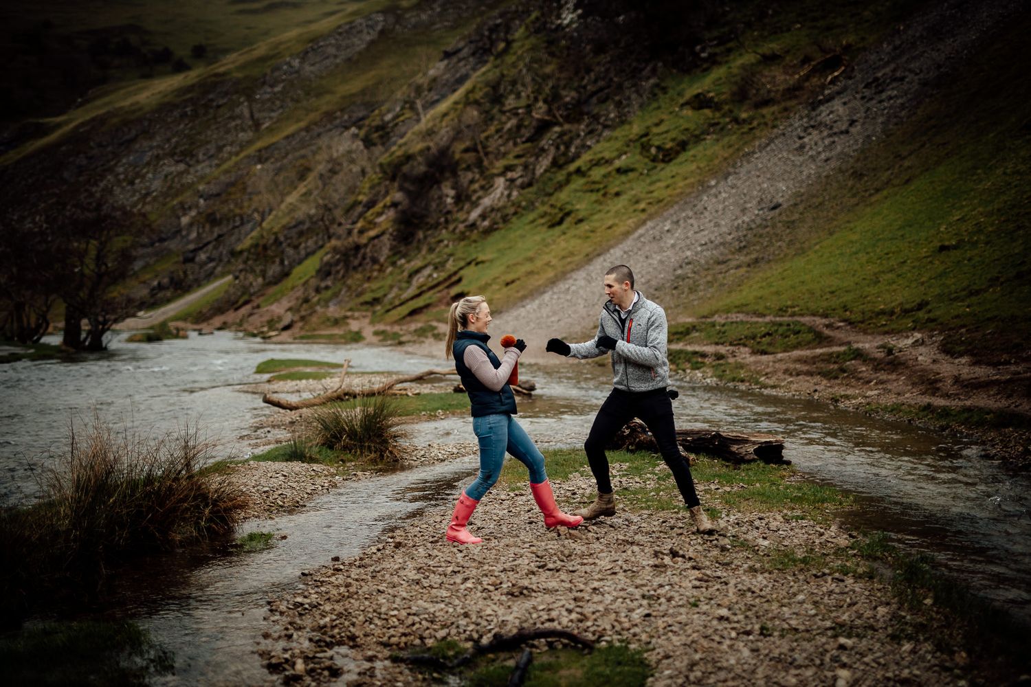People exploring a rocky riverside path in casual outdoor wear.