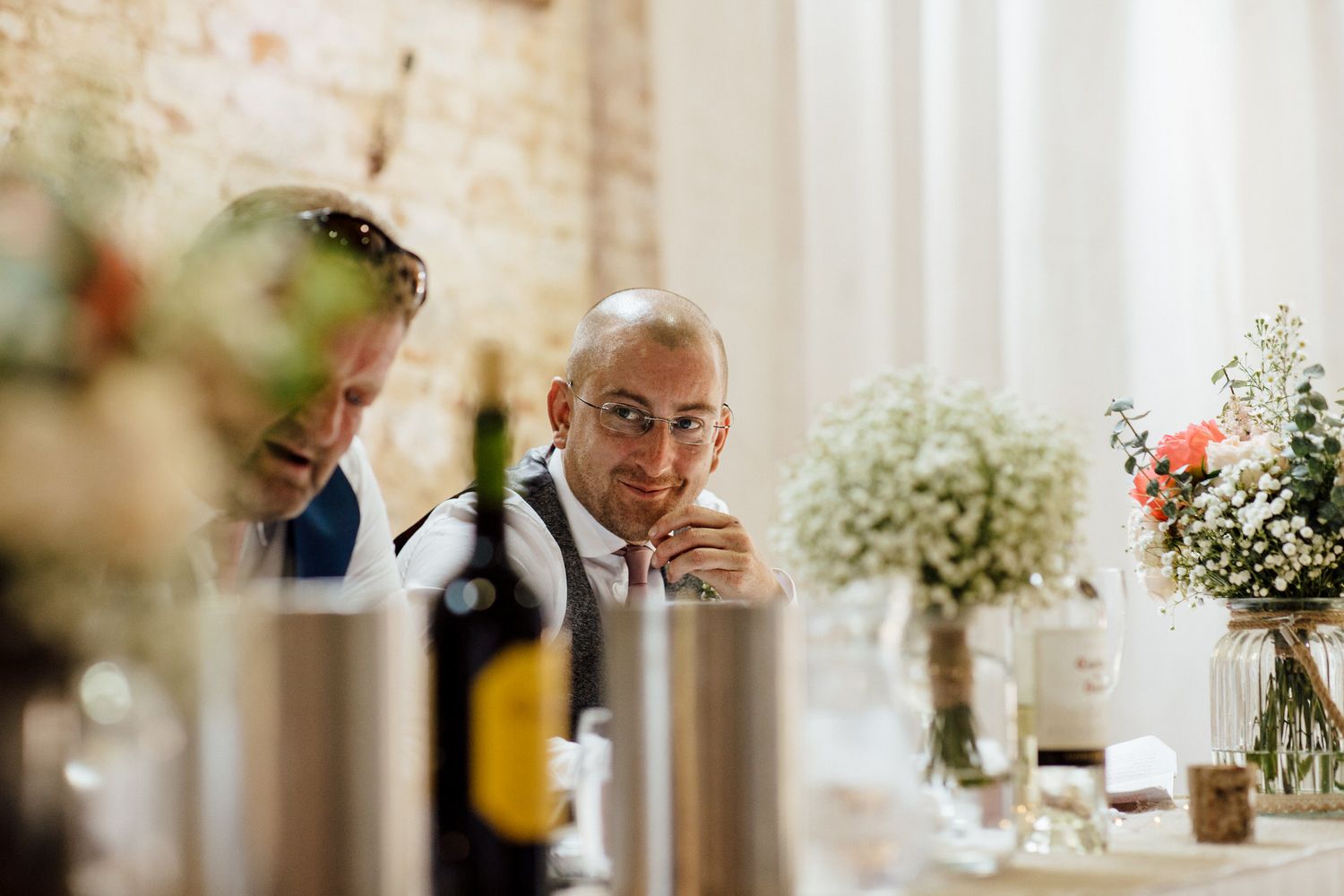 Elegant wedding reception setup with white floral centerpieces and exposed brick walls.