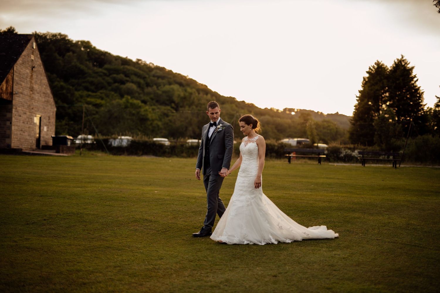 Wedding couple walking together across a scenic green field at sunset.