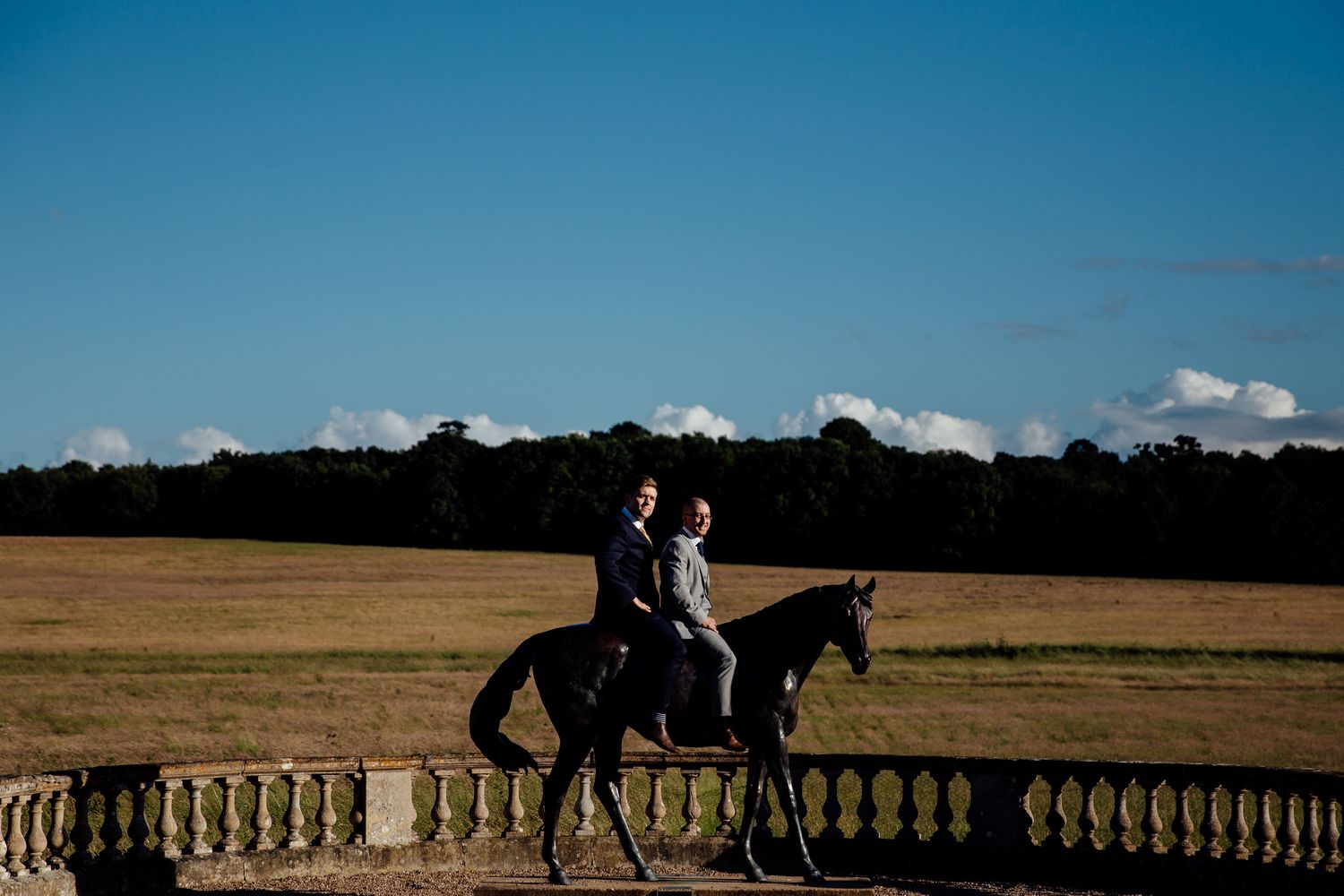 Silhouette of horse and riders against dramatic sky on stone balustrade.