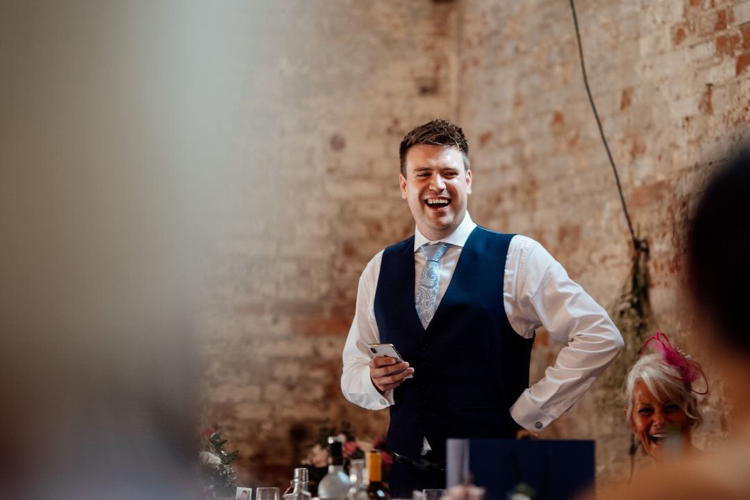 Lively moment during wedding reception speech in rustic brick venue with ambient lighting.