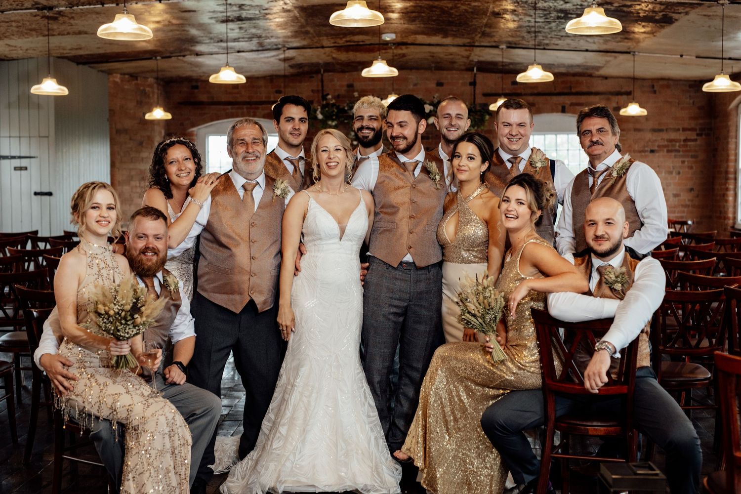 Wedding party group photo in rustic venue with exposed brick walls and industrial lighting.