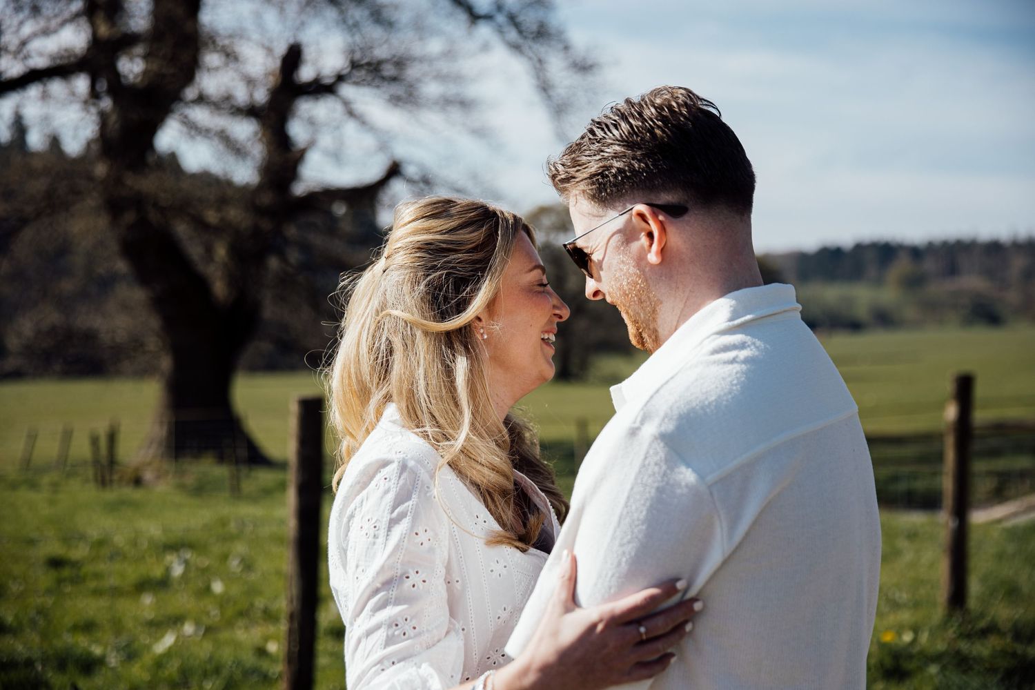 Two people share an intimate moment on a rustic country path surrounded by green fields.