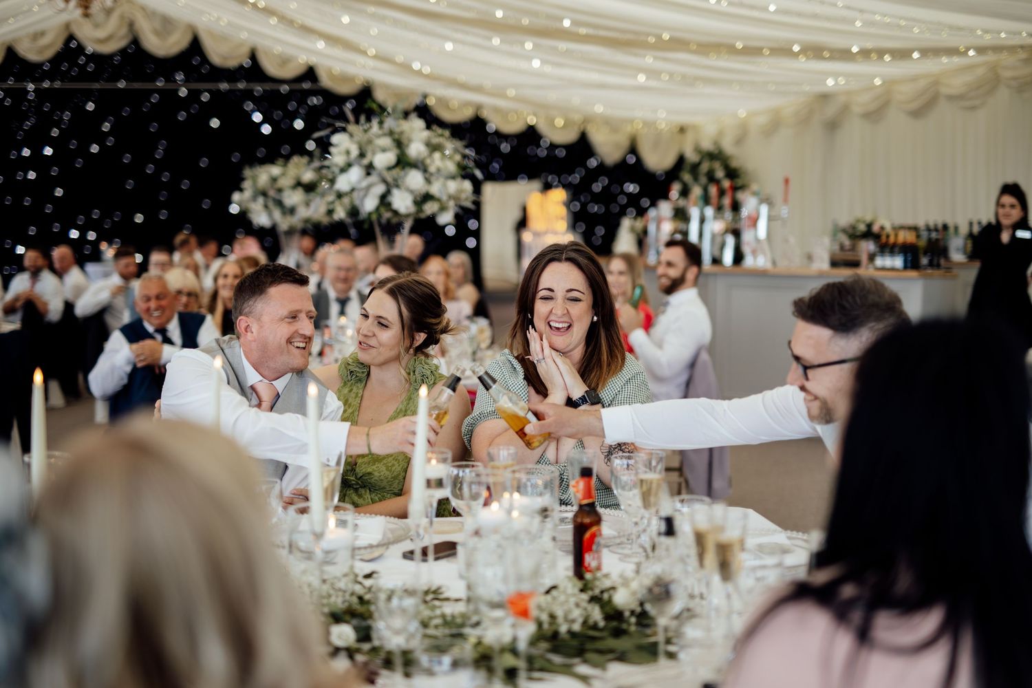 Wedding reception celebration under white tent with fairy lights and floral decor.