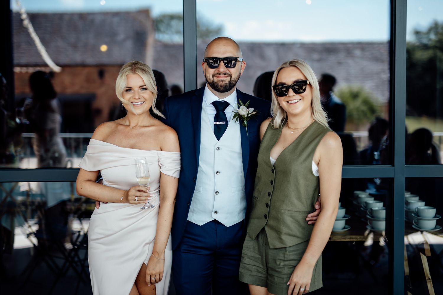 Wedding guests in formal attire pose together at an outdoor venue.