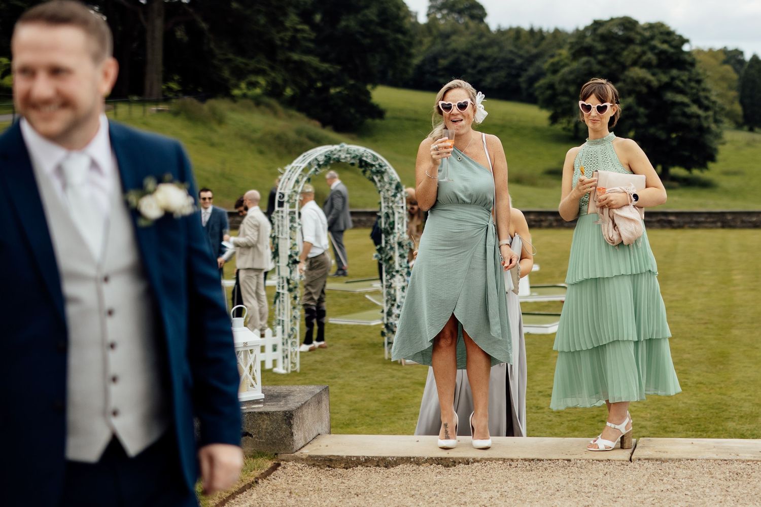 Wedding party members in mint green dresses pose on a sunny lawn.
