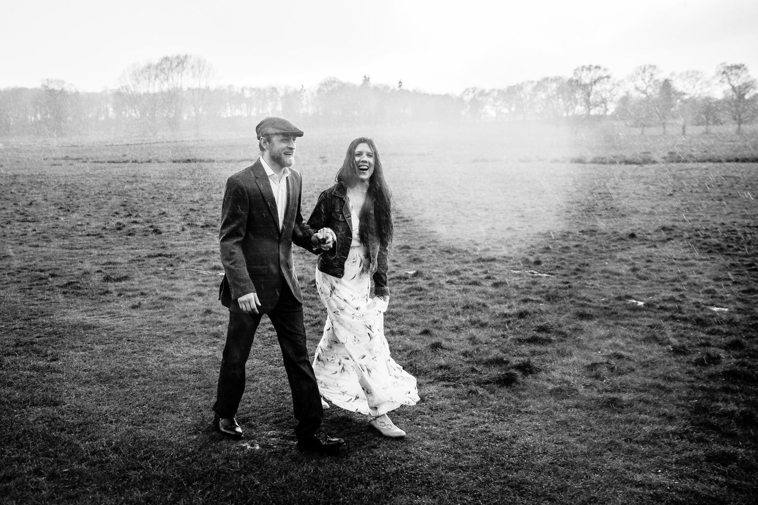 Black and white photo of couple walking together in misty field at sunset.
