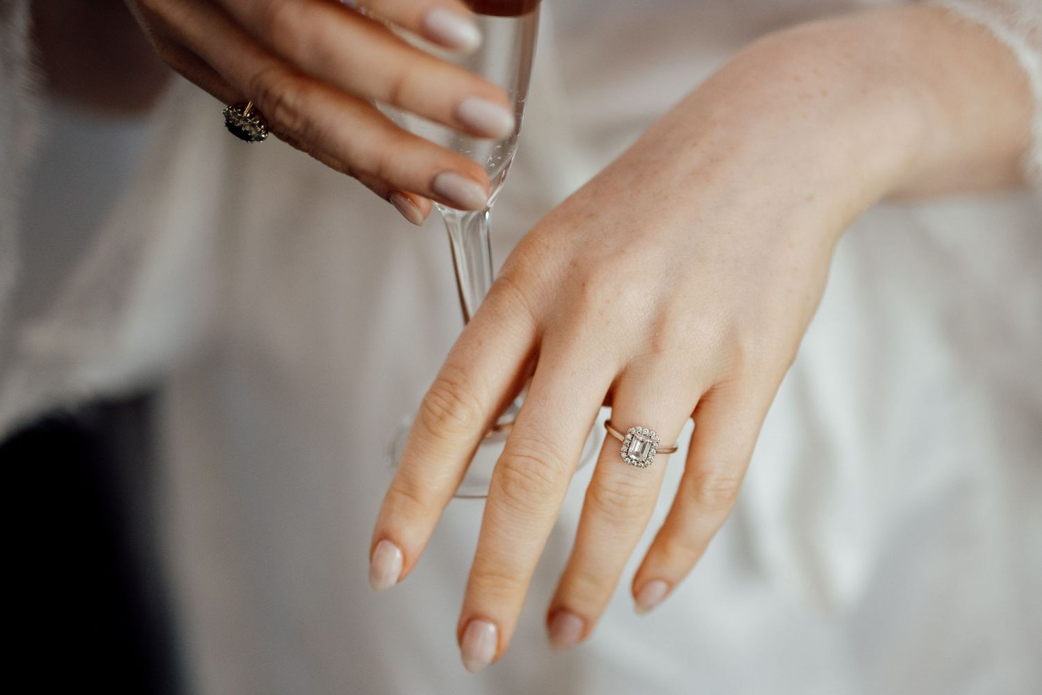 Close-up of engagement ring and wedding band on hand with manicured nails.