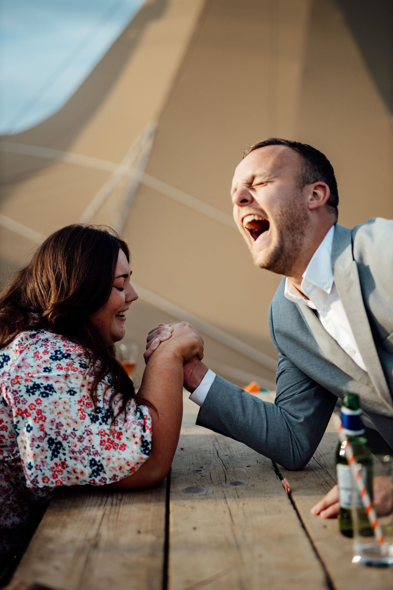 Candid moment of laughter shared across wooden table under tent ceiling.