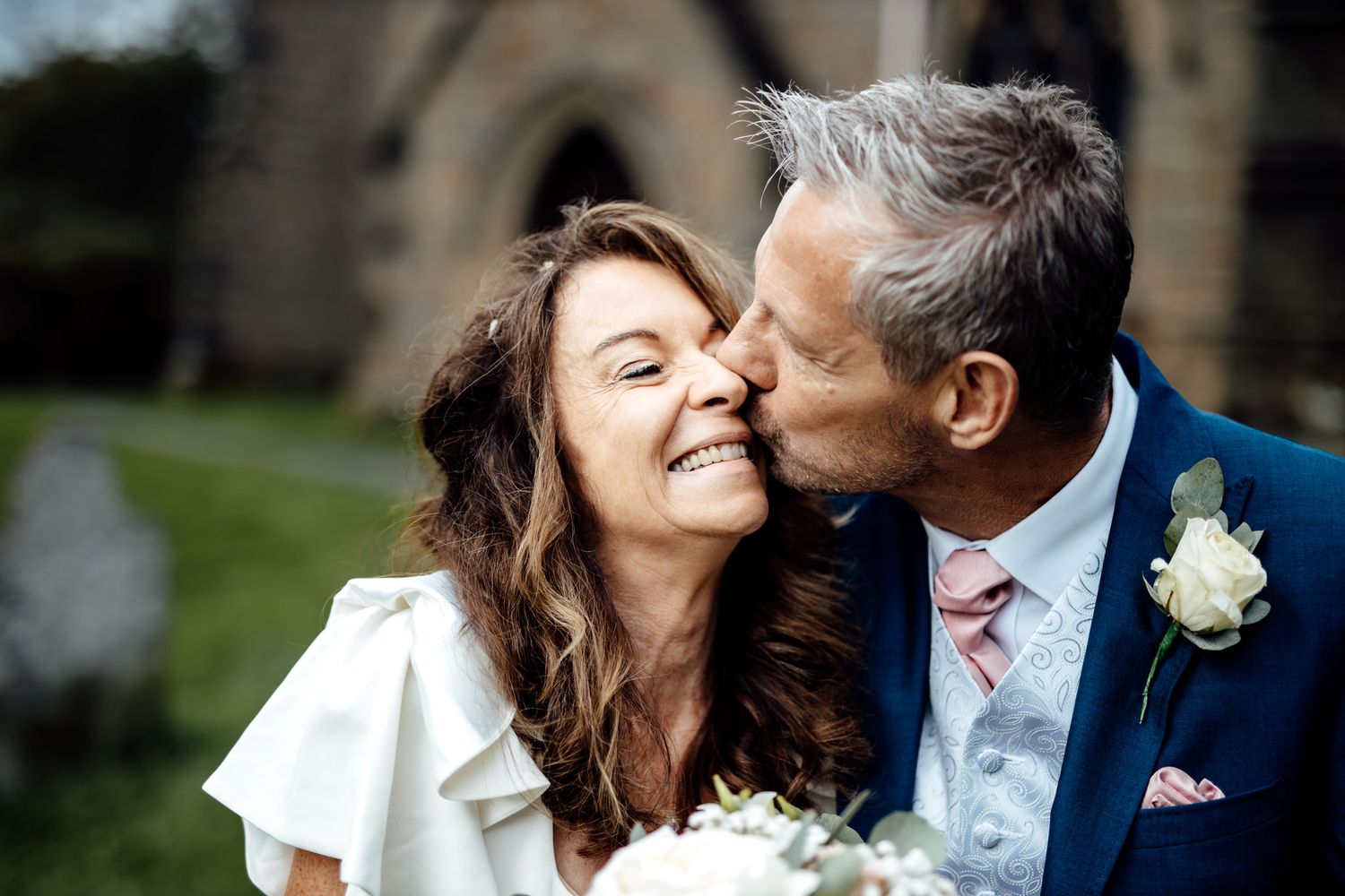 A tender moment shared between a couple in formal wedding attire outdoors.