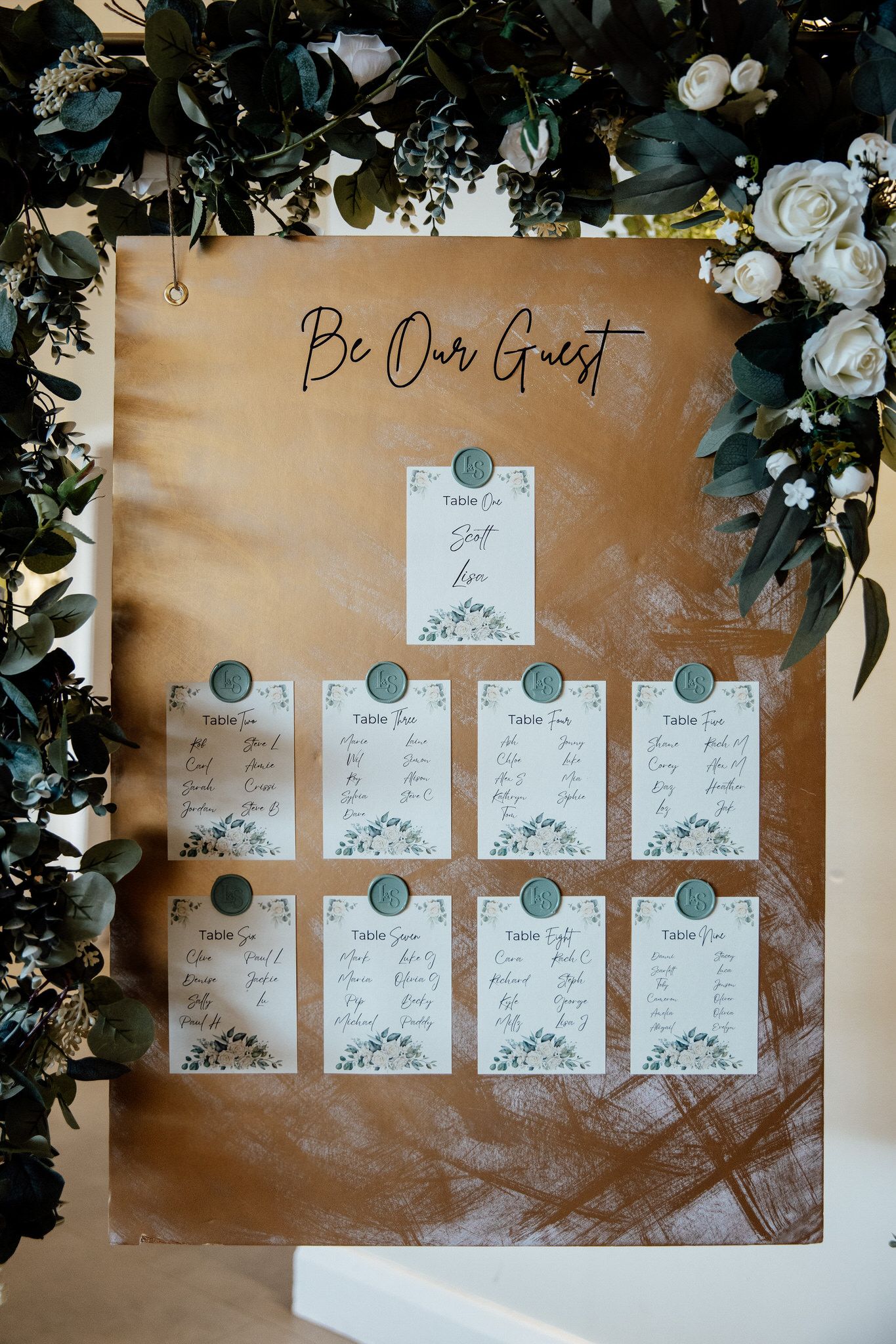 Elegant seating chart display with floral decorations and white cards against a golden backdrop.