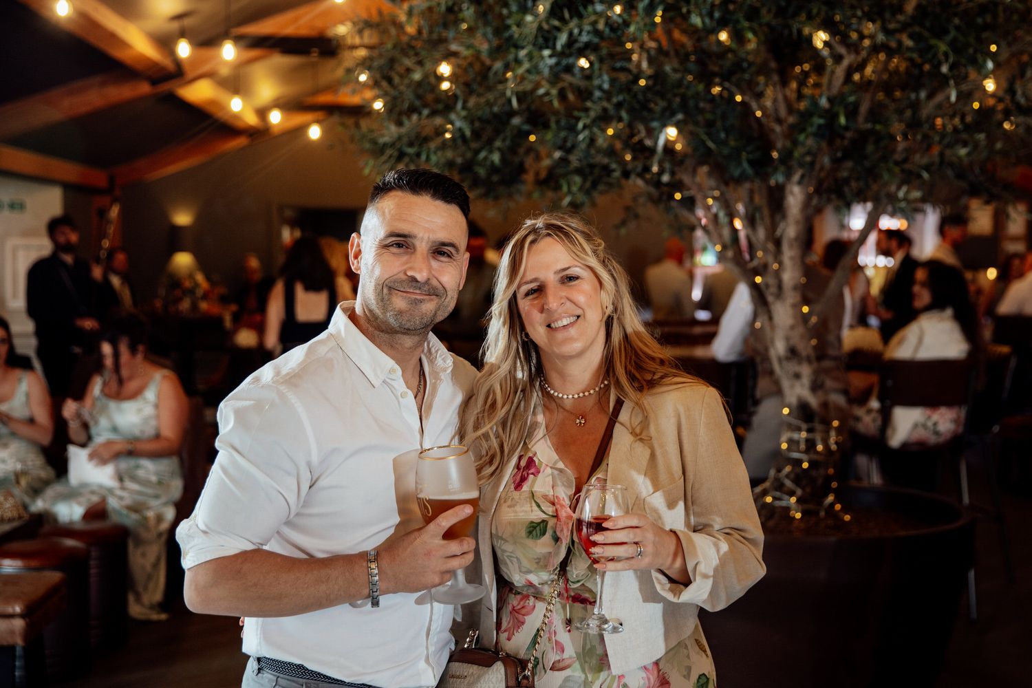 A couple enjoying drinks together at an evening celebration with decorative lighting.