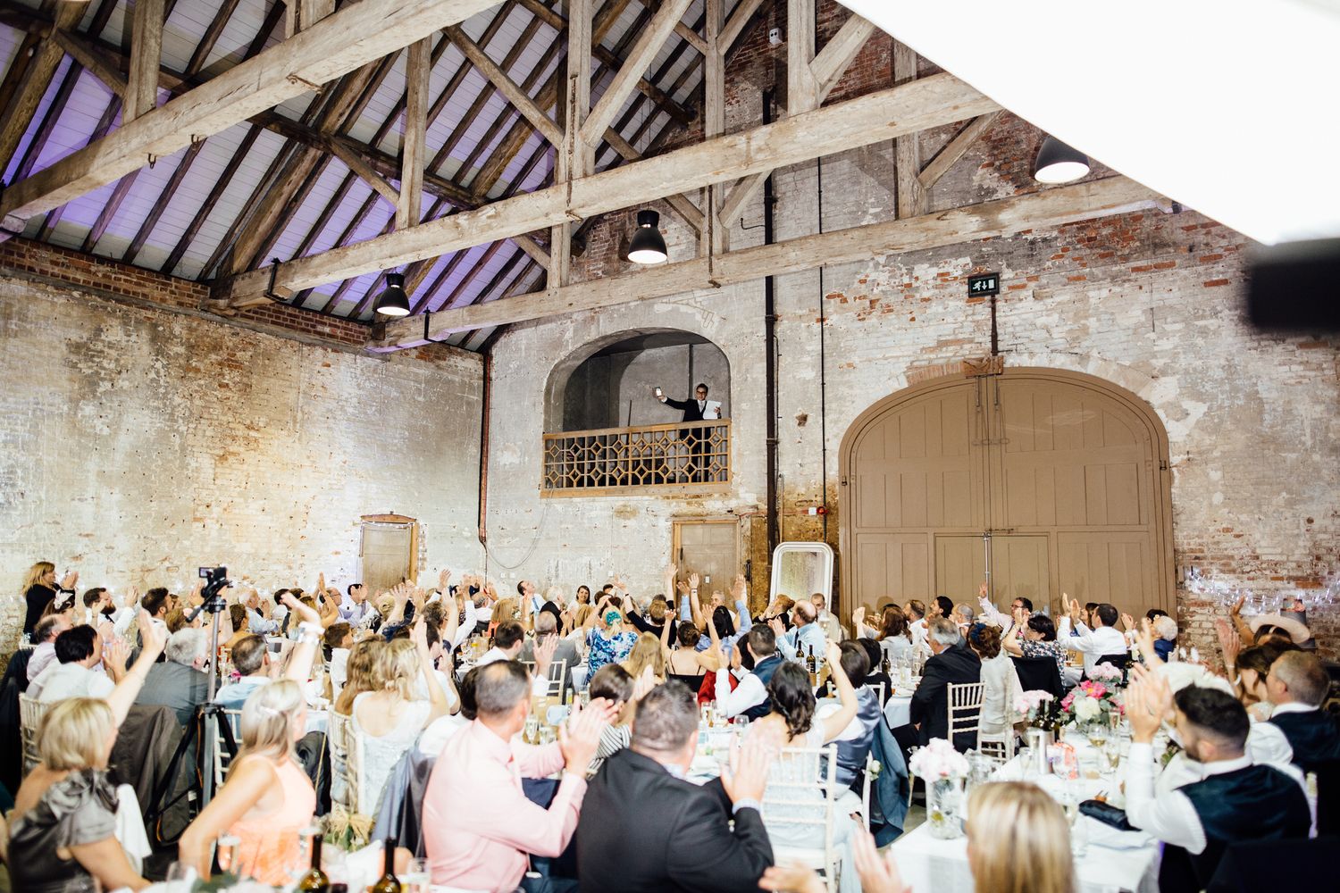 A wide view of wedding reception tables set up in an industrial-style venue with exposed brick walls.