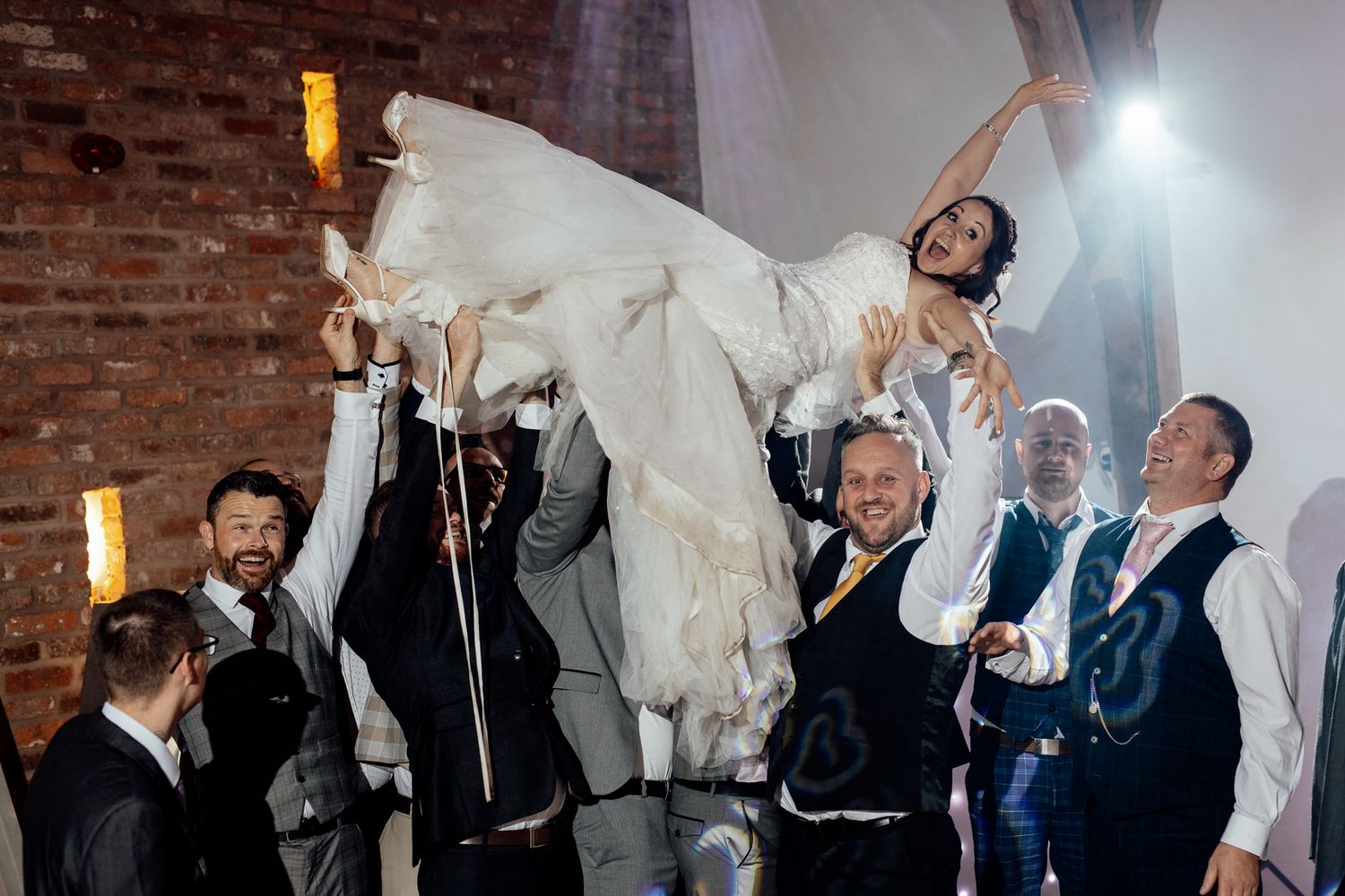 Wedding party celebrating with raised arms against exposed brick wall.