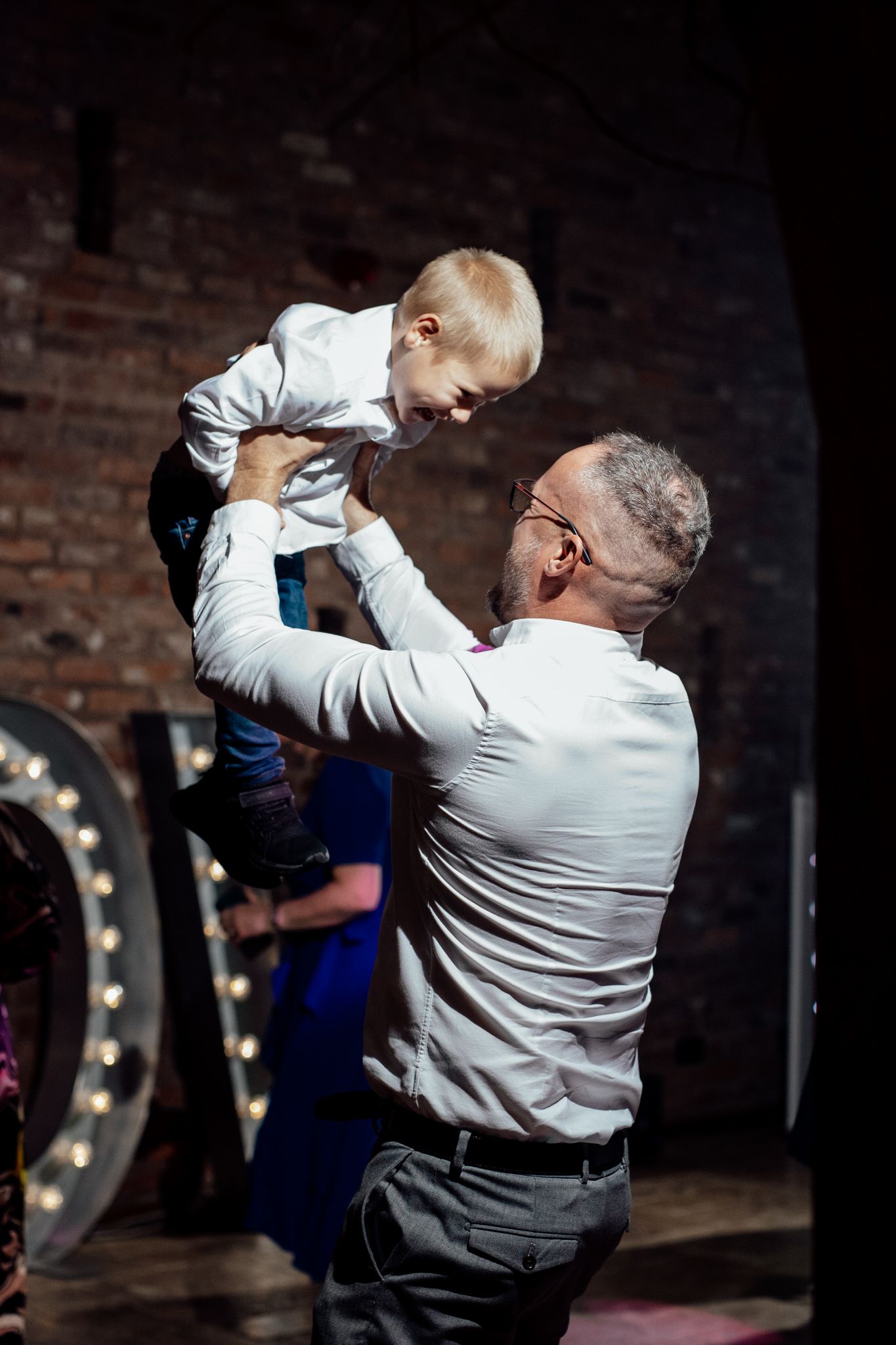 Joyful dance floor moment captured during wedding reception with dramatic lighting and brick wall backdrop.
