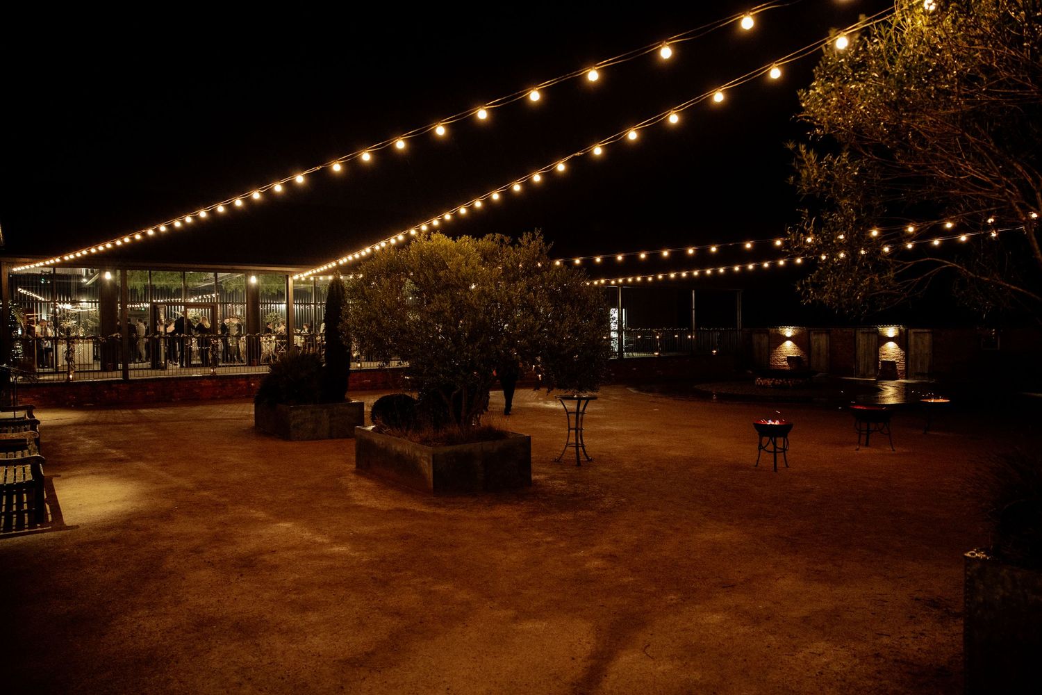 Outdoor patio with string lights illuminating tables and seating at night.