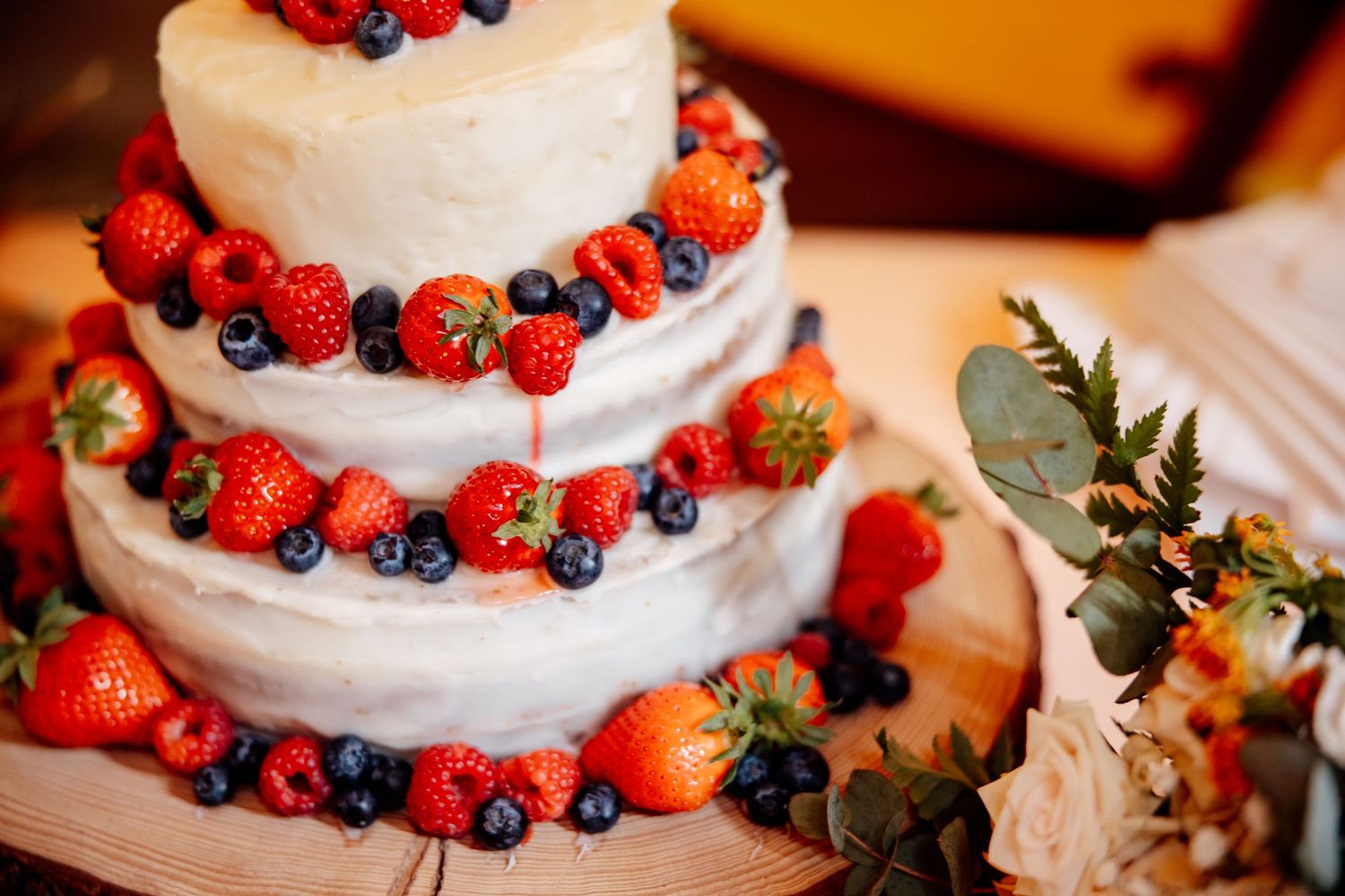 Three-tiered white wedding cake decorated with fresh strawberries, blueberries and raspberries in a rustic style.
