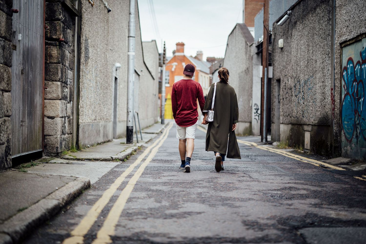 Two people walking down an urban alleyway with white walls.