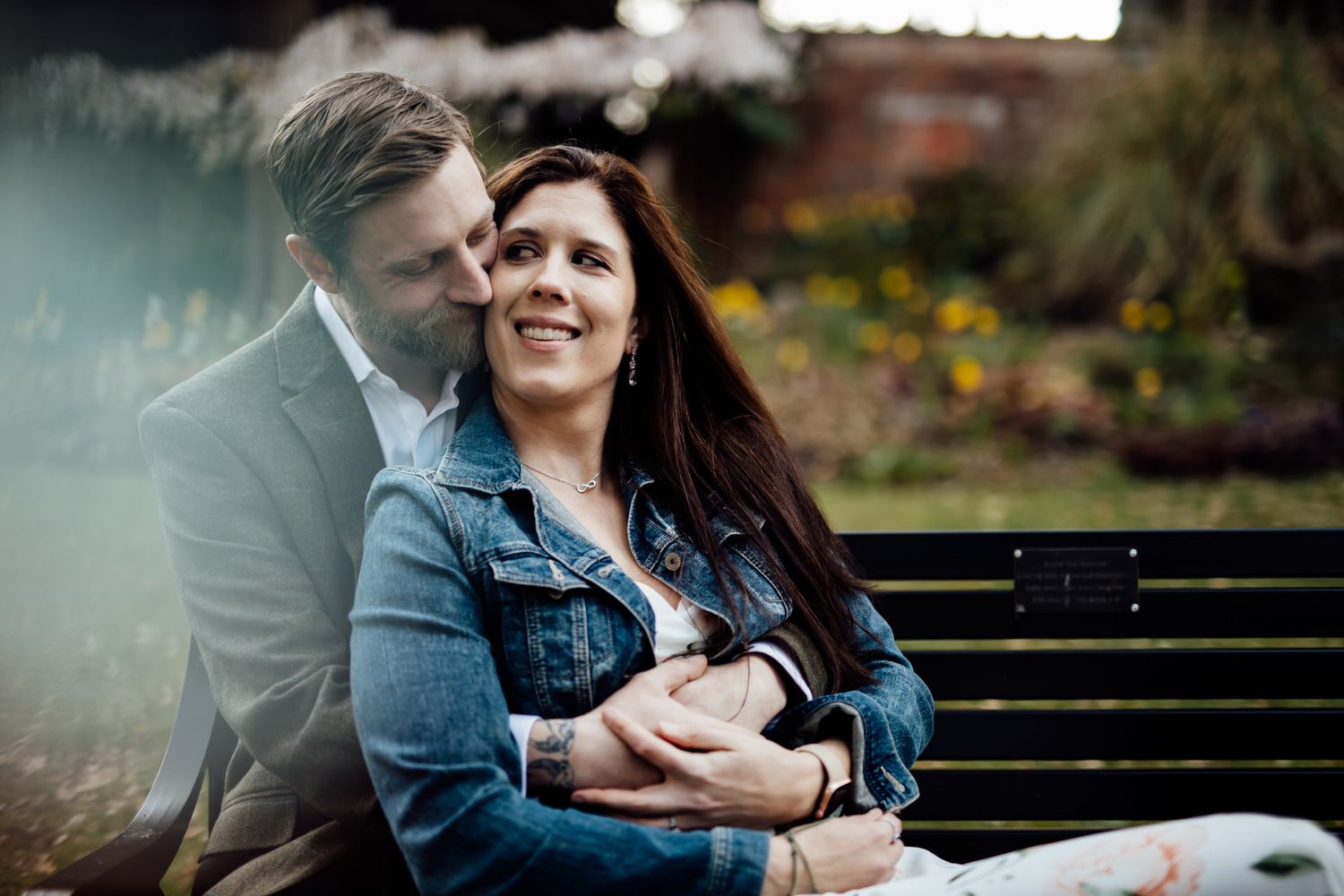 Couple sitting close together on park bench during outdoor photoshoot.