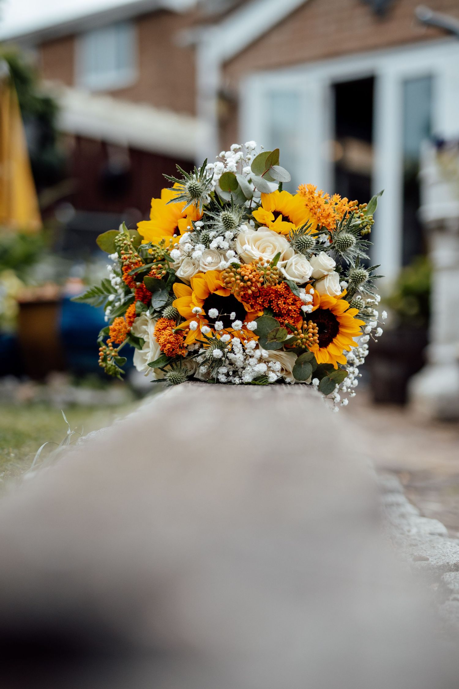 Vibrant wedding bouquet featuring sunflowers, white flowers and greenery against blurred background.