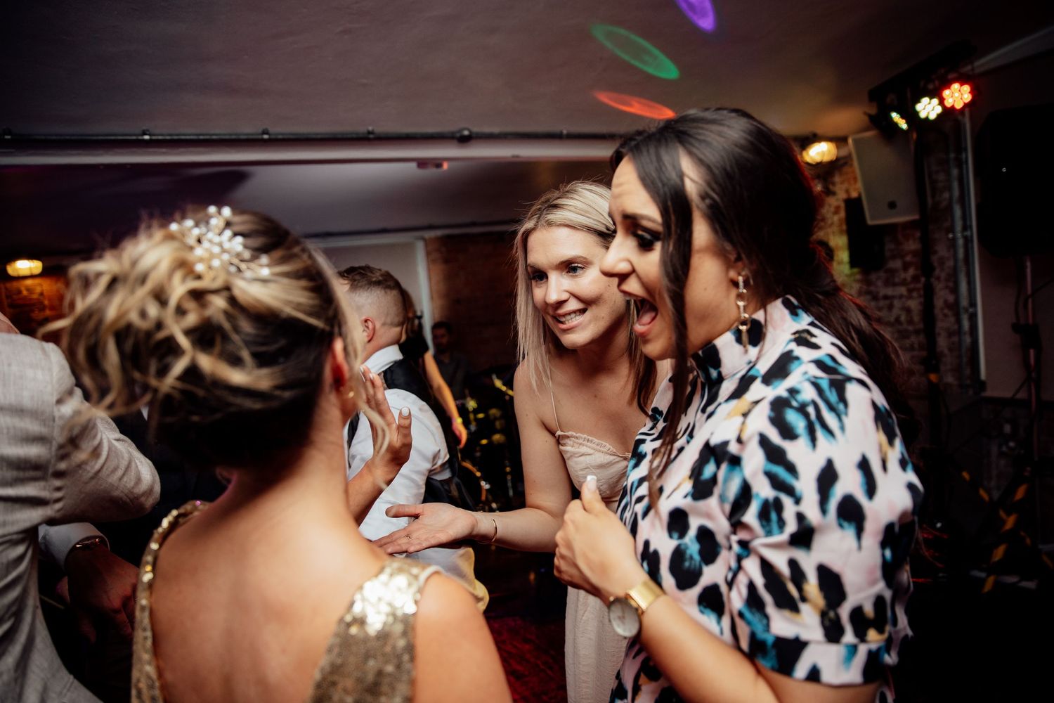 Wedding reception dance floor filled with guests dancing under colorful lighting.