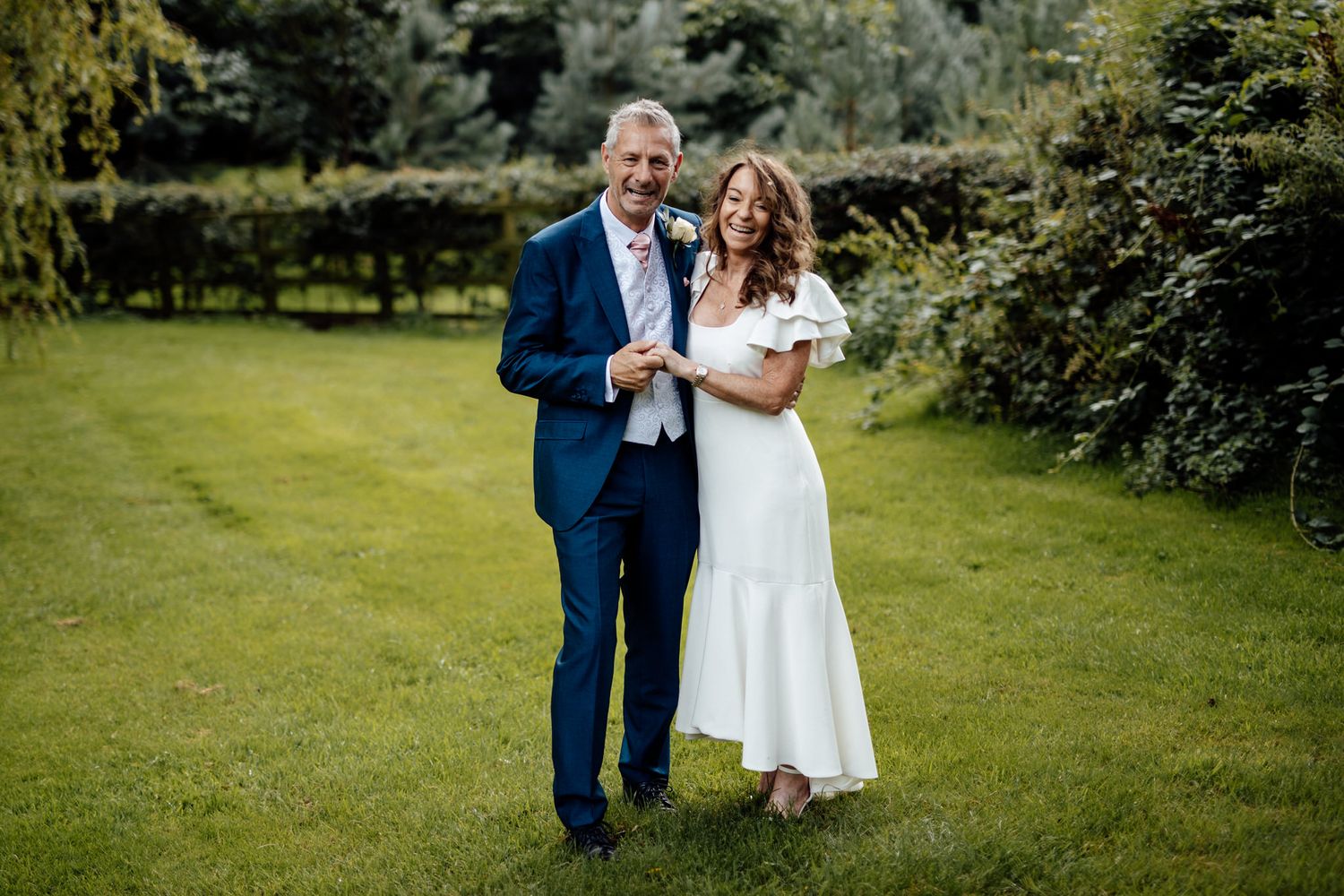 A couple shares a joyful moment together on a lush green lawn during their wedding day celebration.