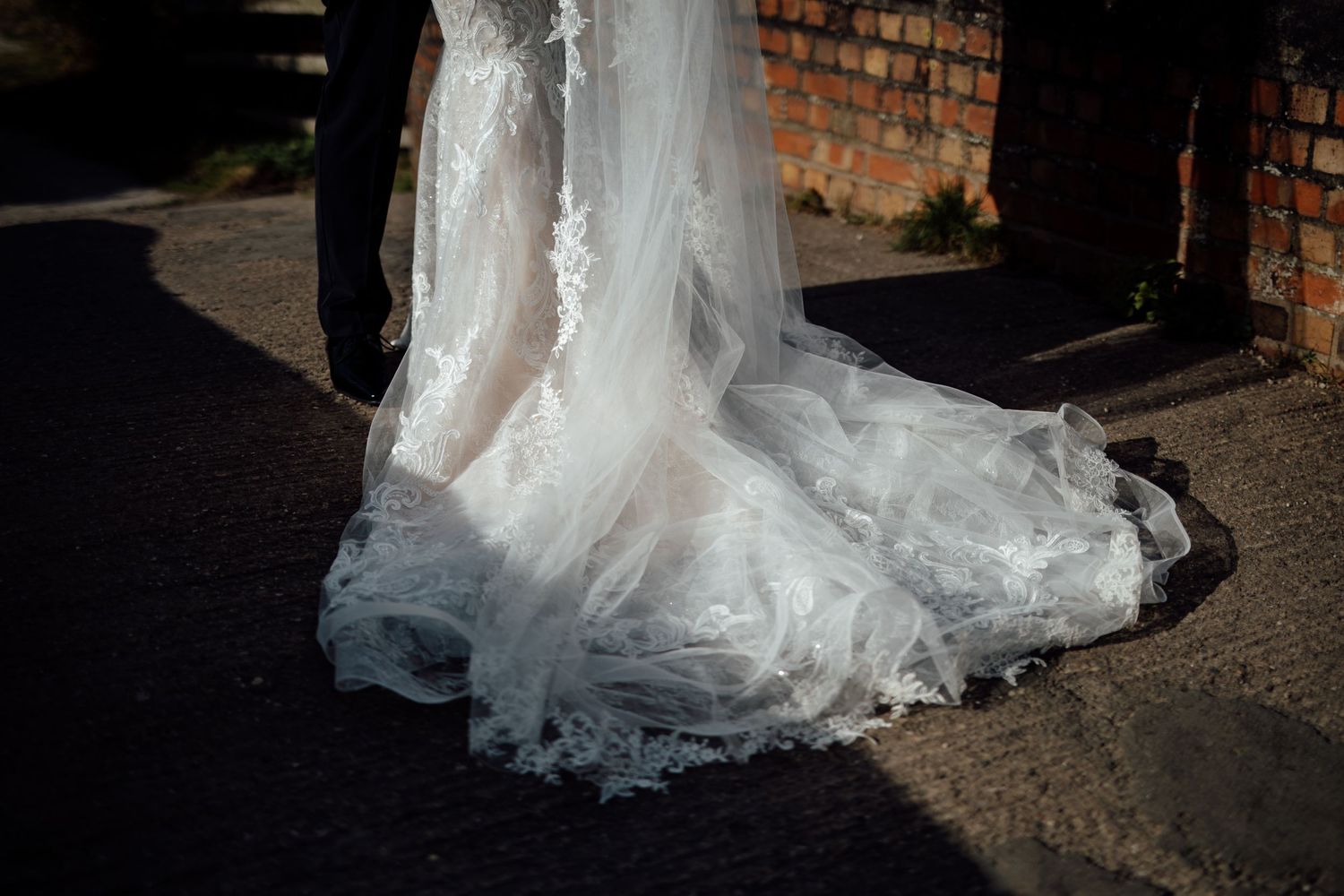 Close-up detail of an intricate lace wedding dress train trailing on stone ground.