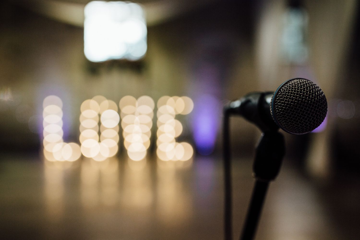 A microphone stands in front of blurred LOVE marquee letters at an event venue.