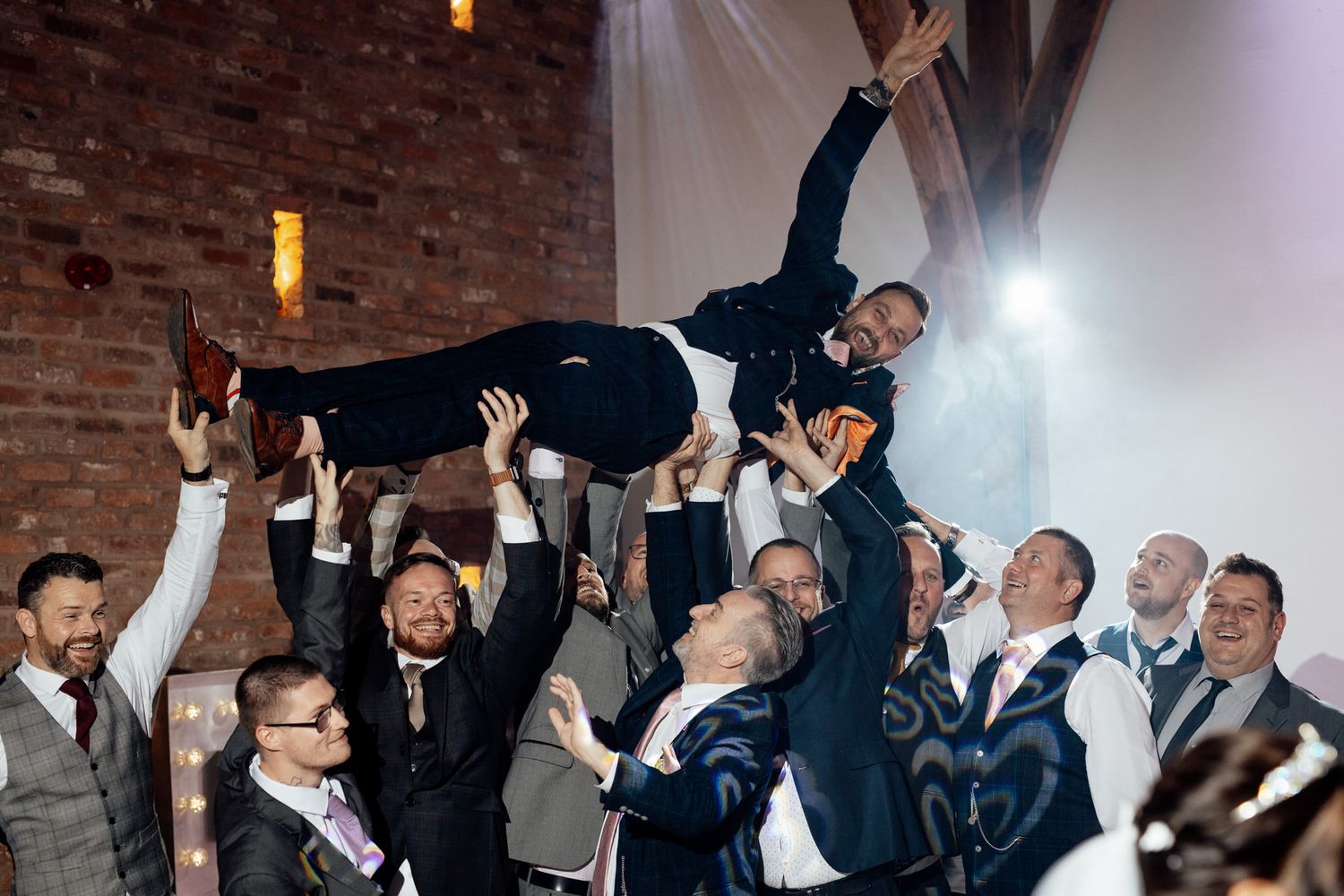 Wedding guests celebrate on the dance floor with hands raised in joyful excitement at an indoor reception.