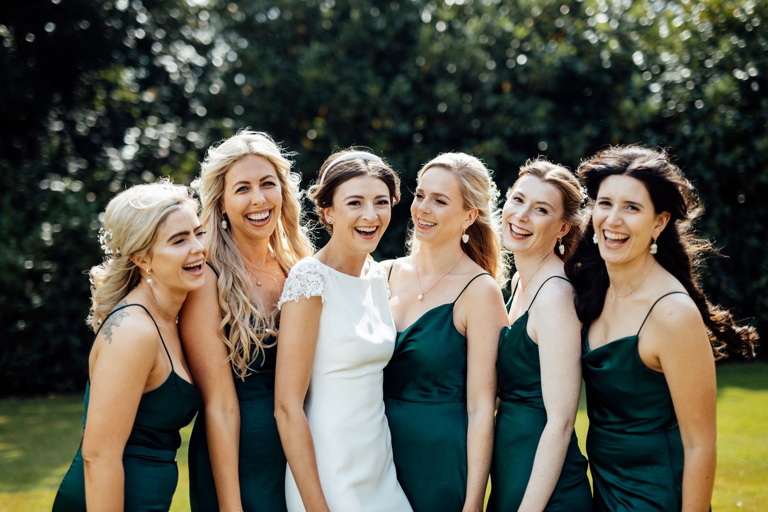 Bridal party sharing a candid laughing moment in matching emerald green dresses.