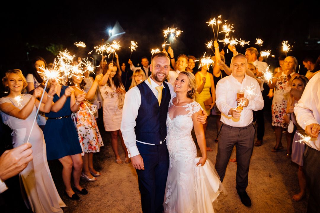 Wedding guests hold sparklers creating magical light trails during nighttime celebration.