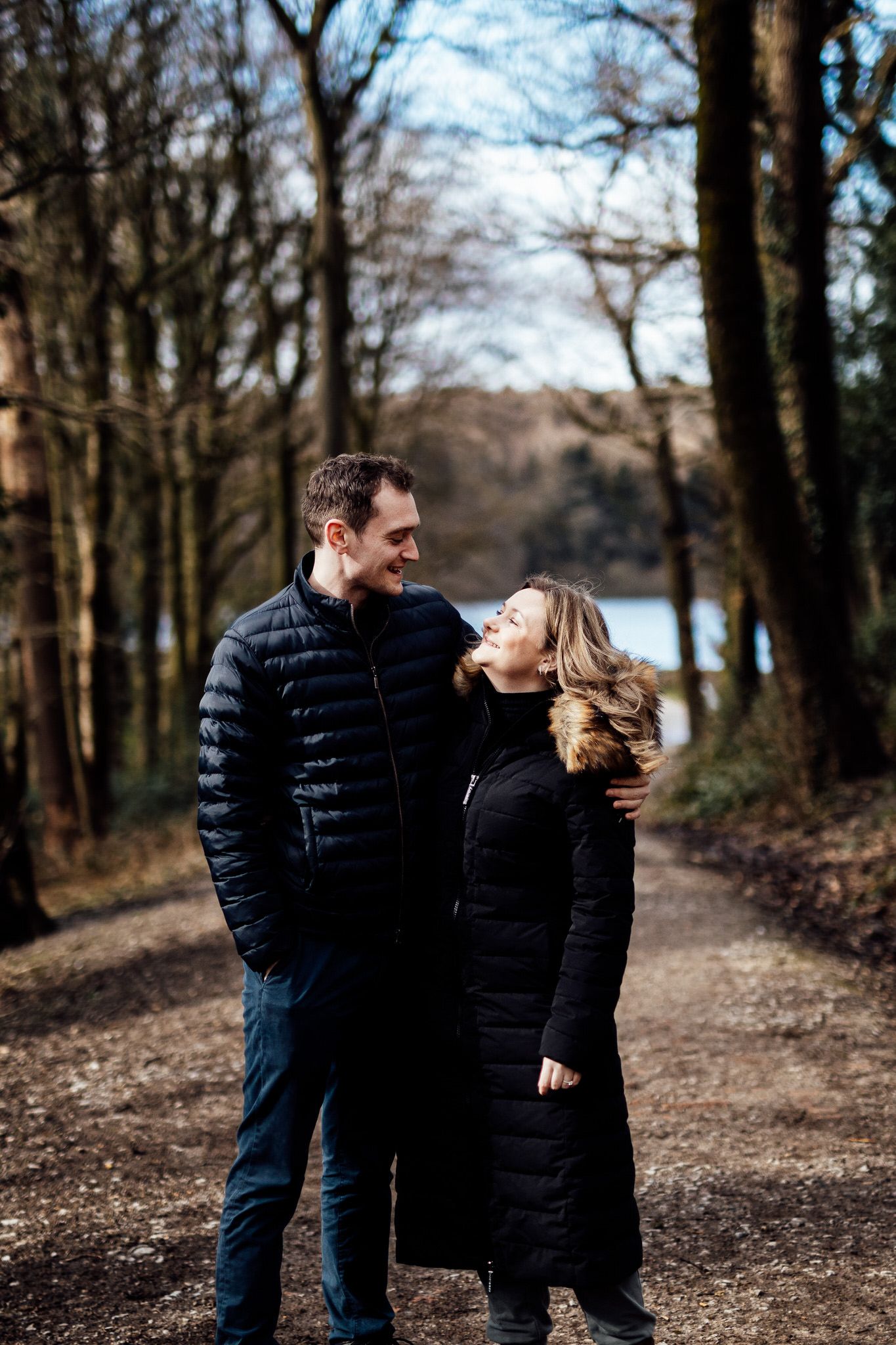 Couple in matching black coats sharing a tender moment on a forest trail.