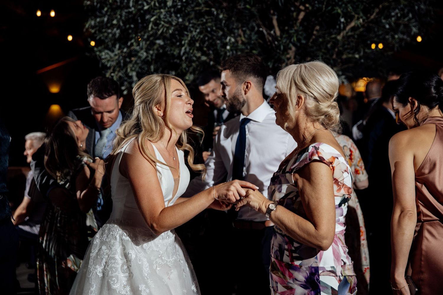 Wedding guests dancing together on a dimly lit dance floor at an evening reception celebration.