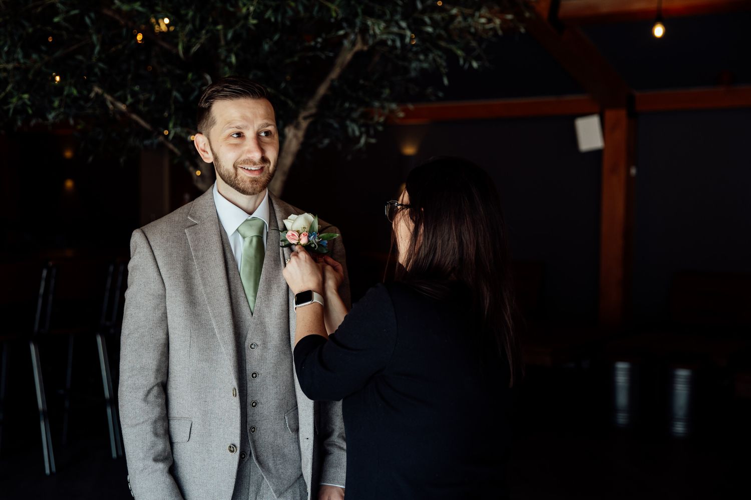 A boutonniere being pinned on a light gray suit at a wedding.
