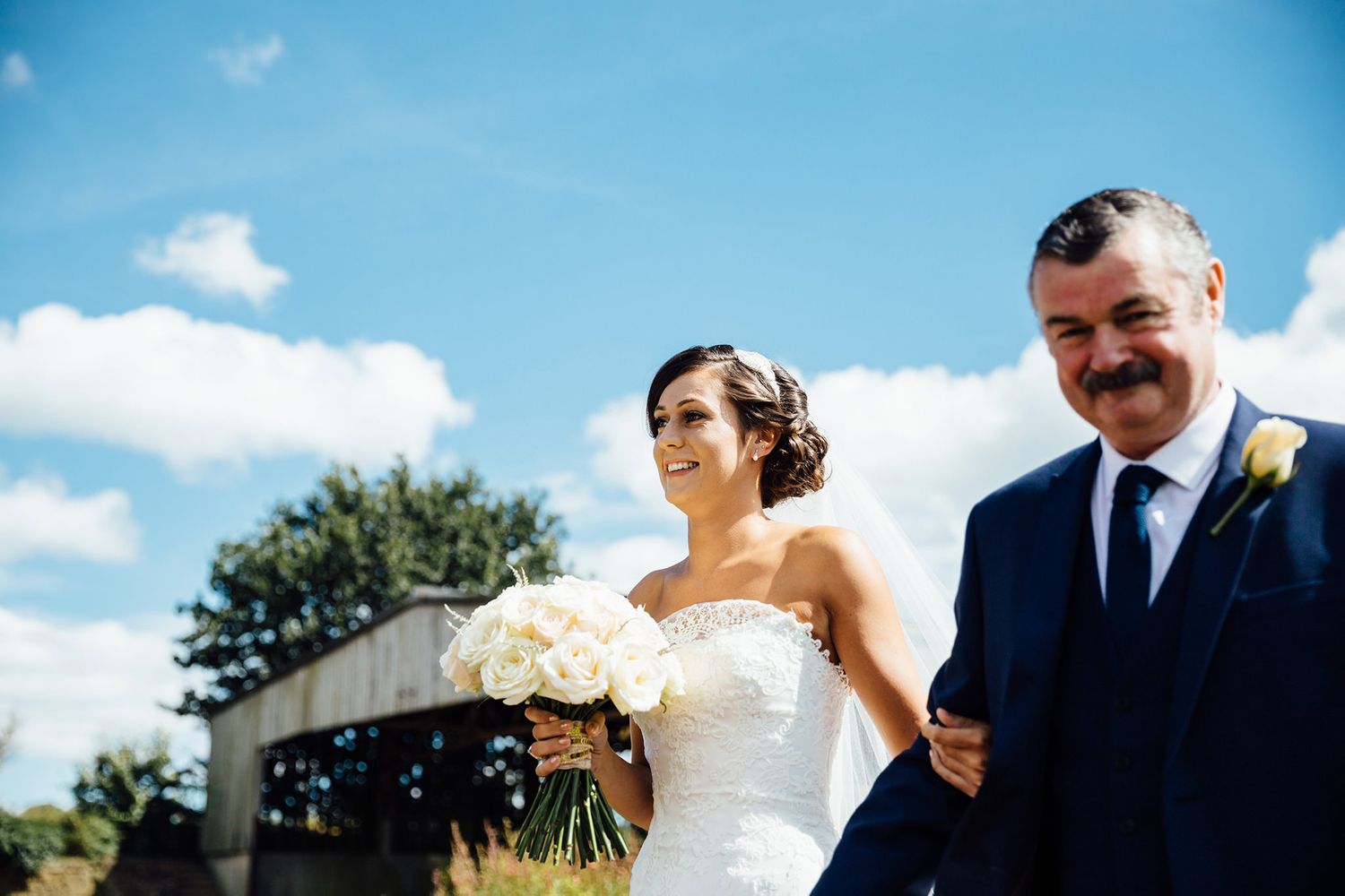 Wedding party poses against a bright blue sky on a sunny summer day.