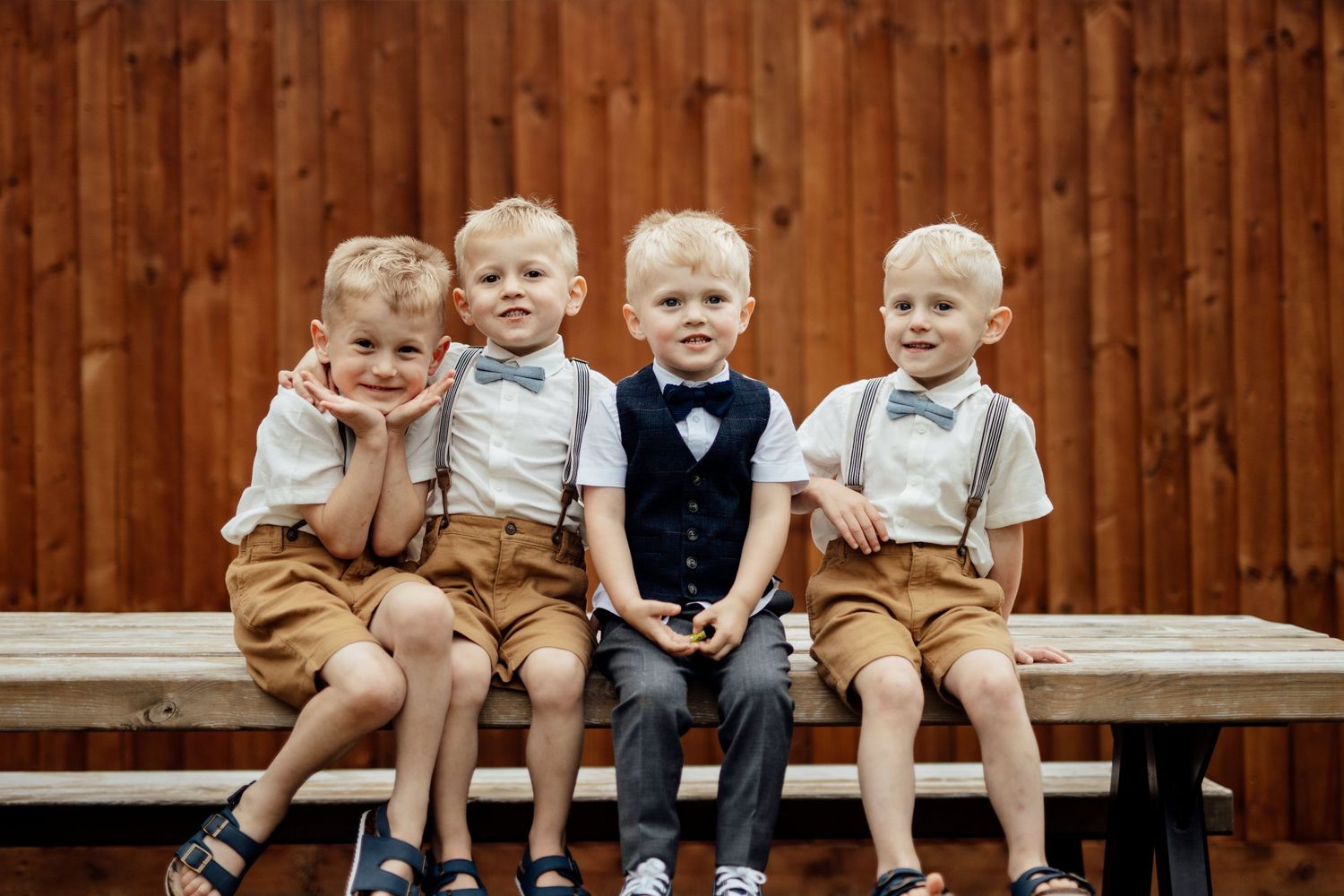 Young children in formal attire sitting on wooden bench at wedding.