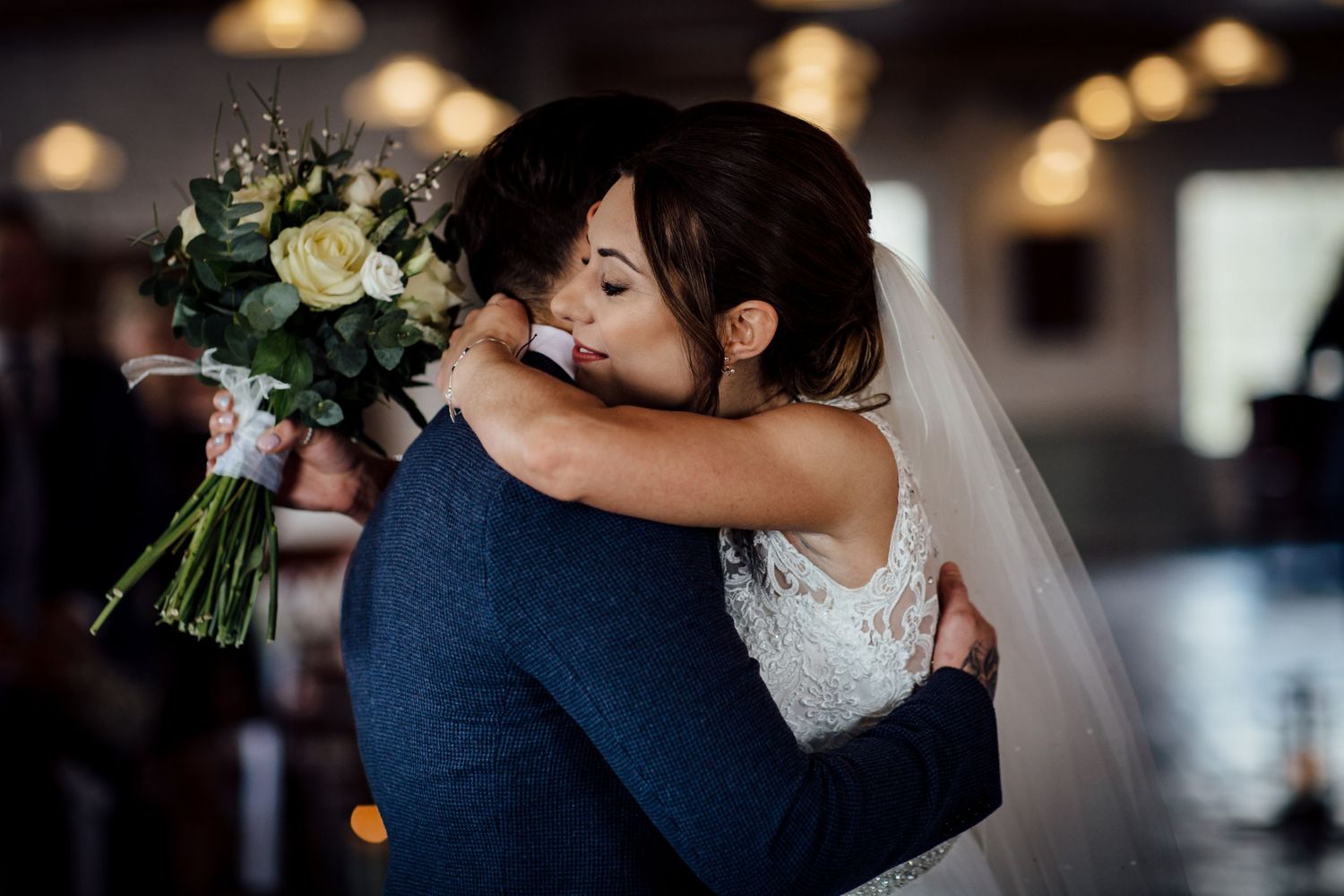 Intimate wedding ceremony moment with couple embracing in front of warm ambient lighting.