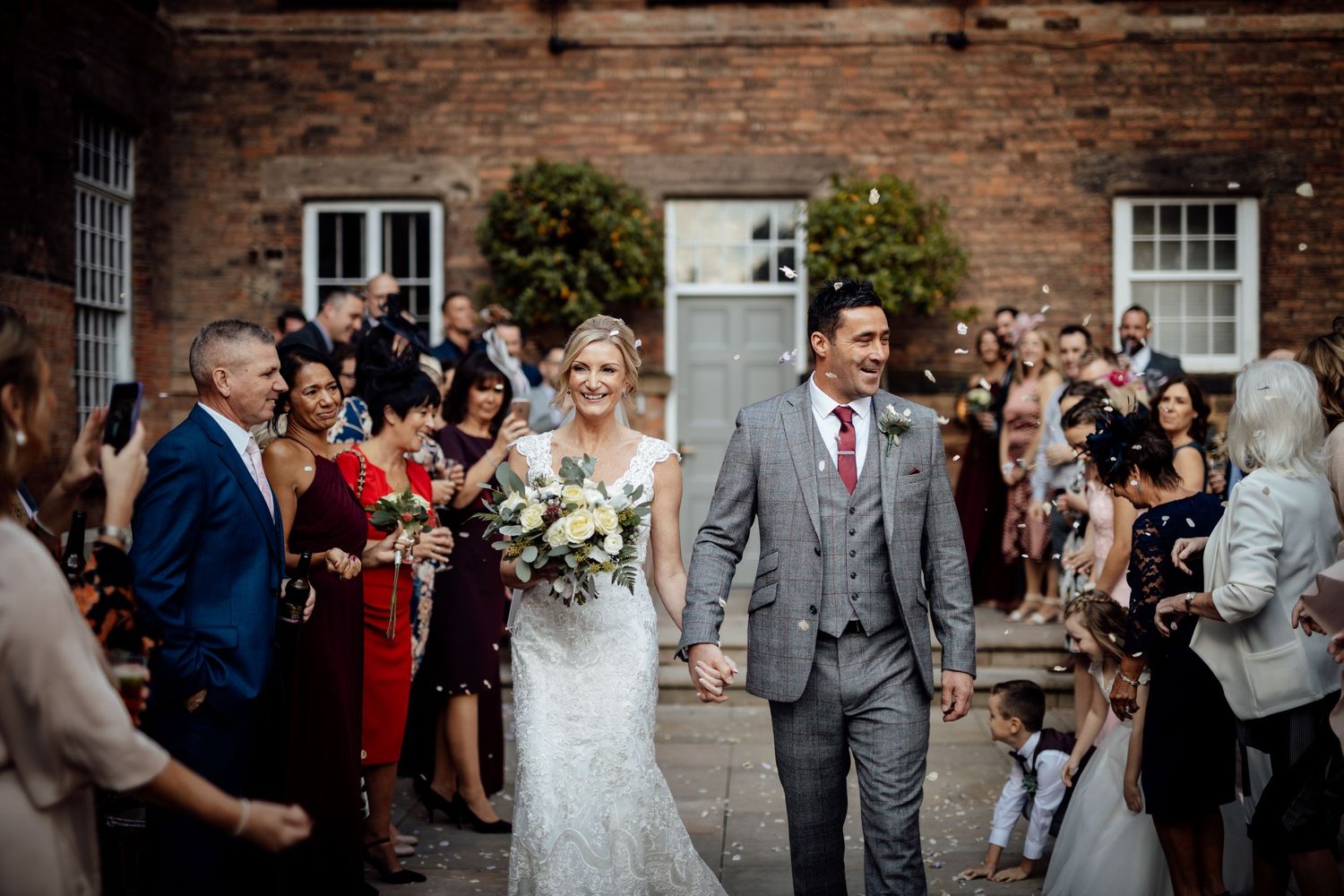 Wedding party and guests gathered outside historic brick building during celebration.