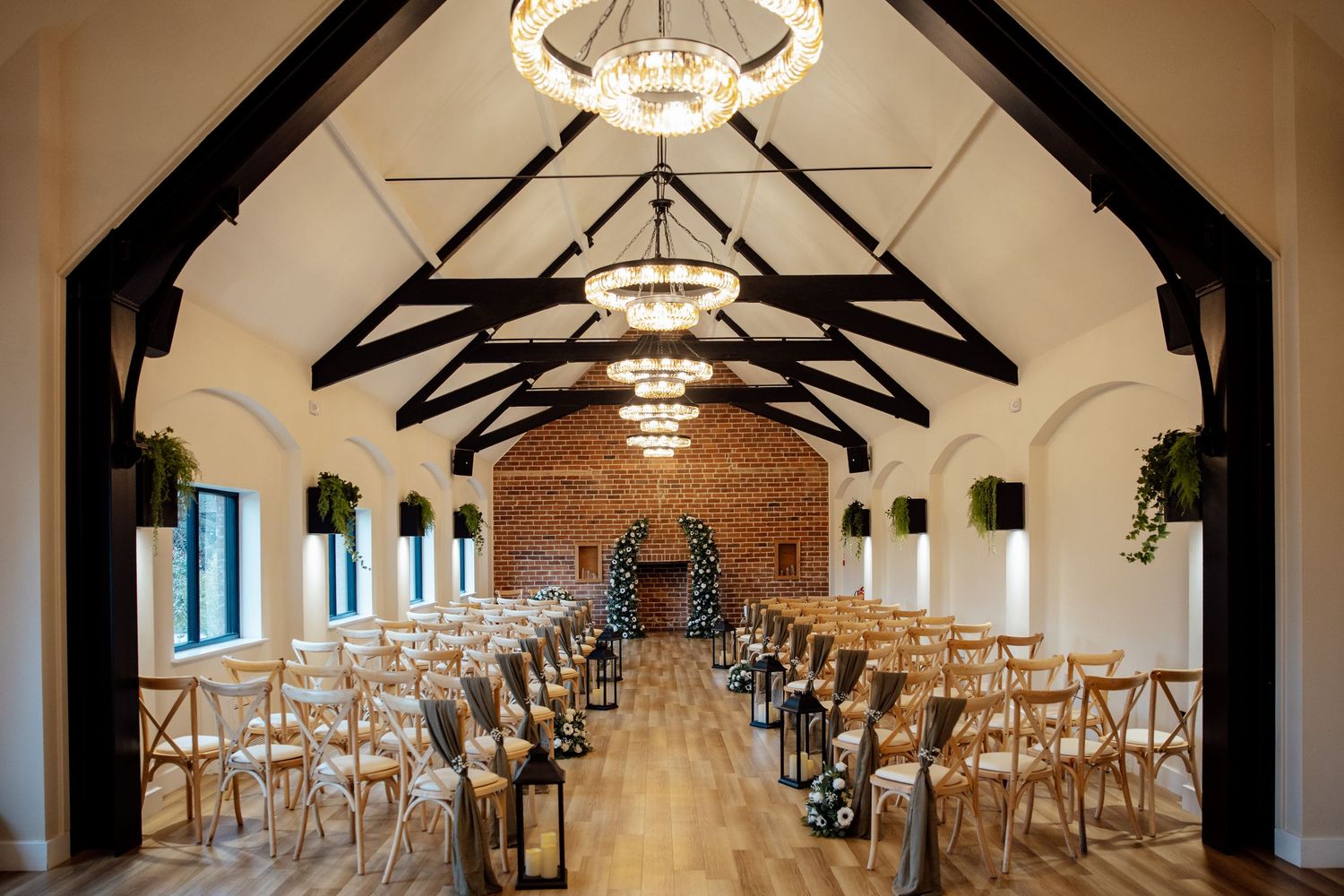 Elegant wedding venue with vaulted ceilings, chandelier lighting, exposed brick, and wooden chairs arranged for a ceremony.